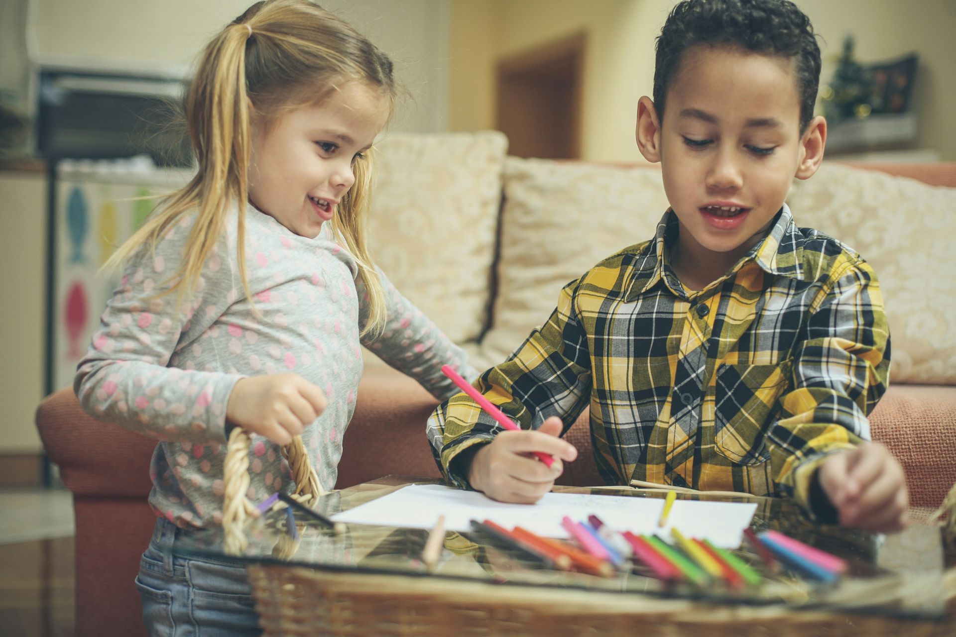 A boy and a girl are sitting at a table drawing with colored pencils.