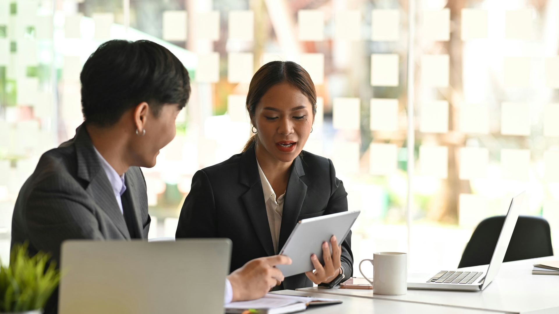 A man and a woman are sitting at a table looking at a tablet.