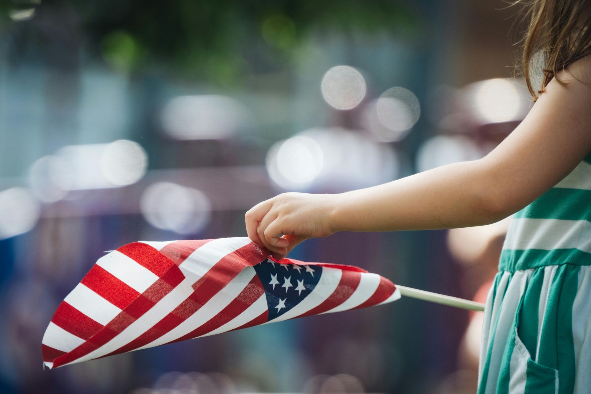 A little girl is holding an american flag in her hand.