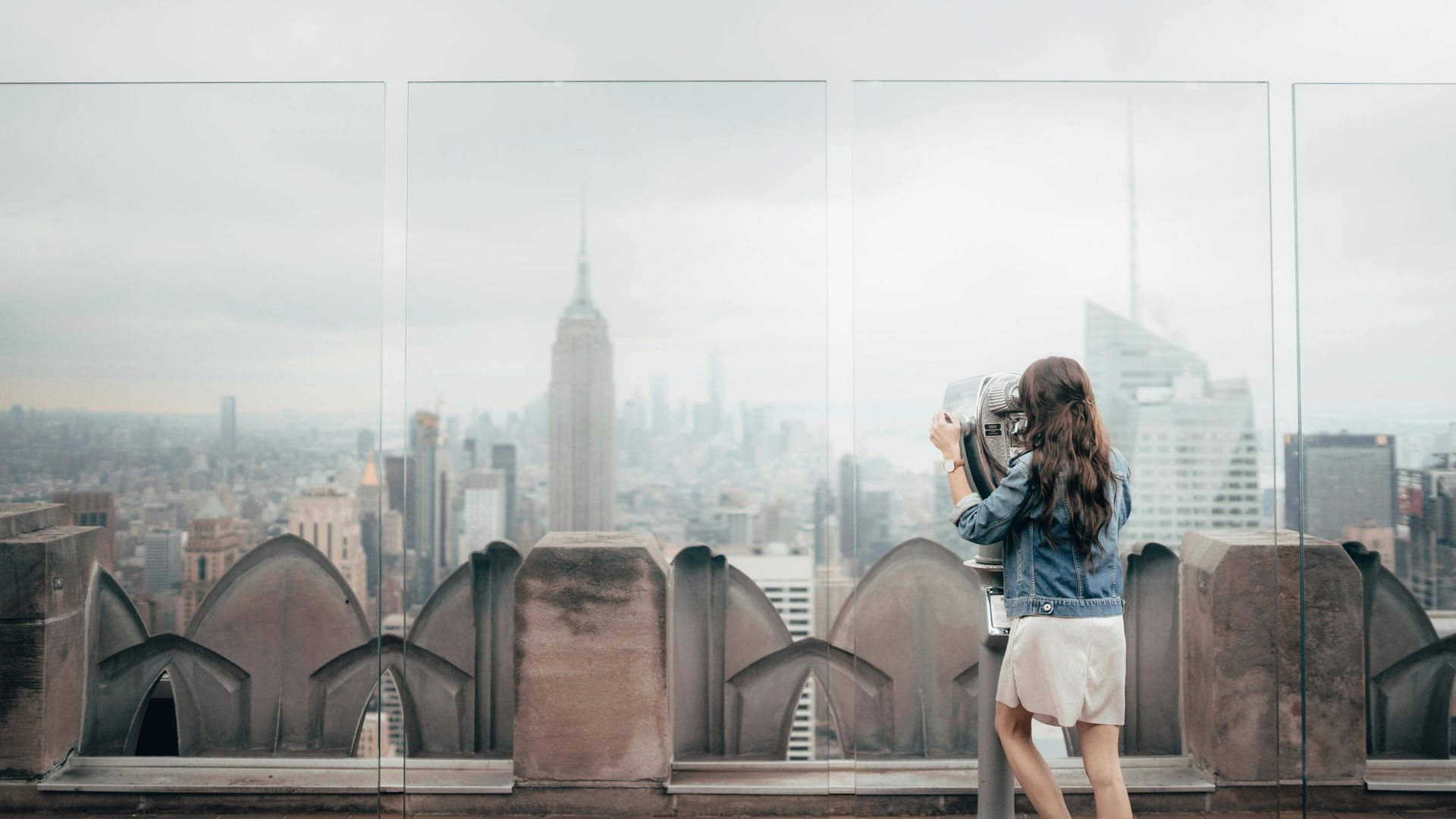 A woman is taking a picture of the city skyline from the top of a building.