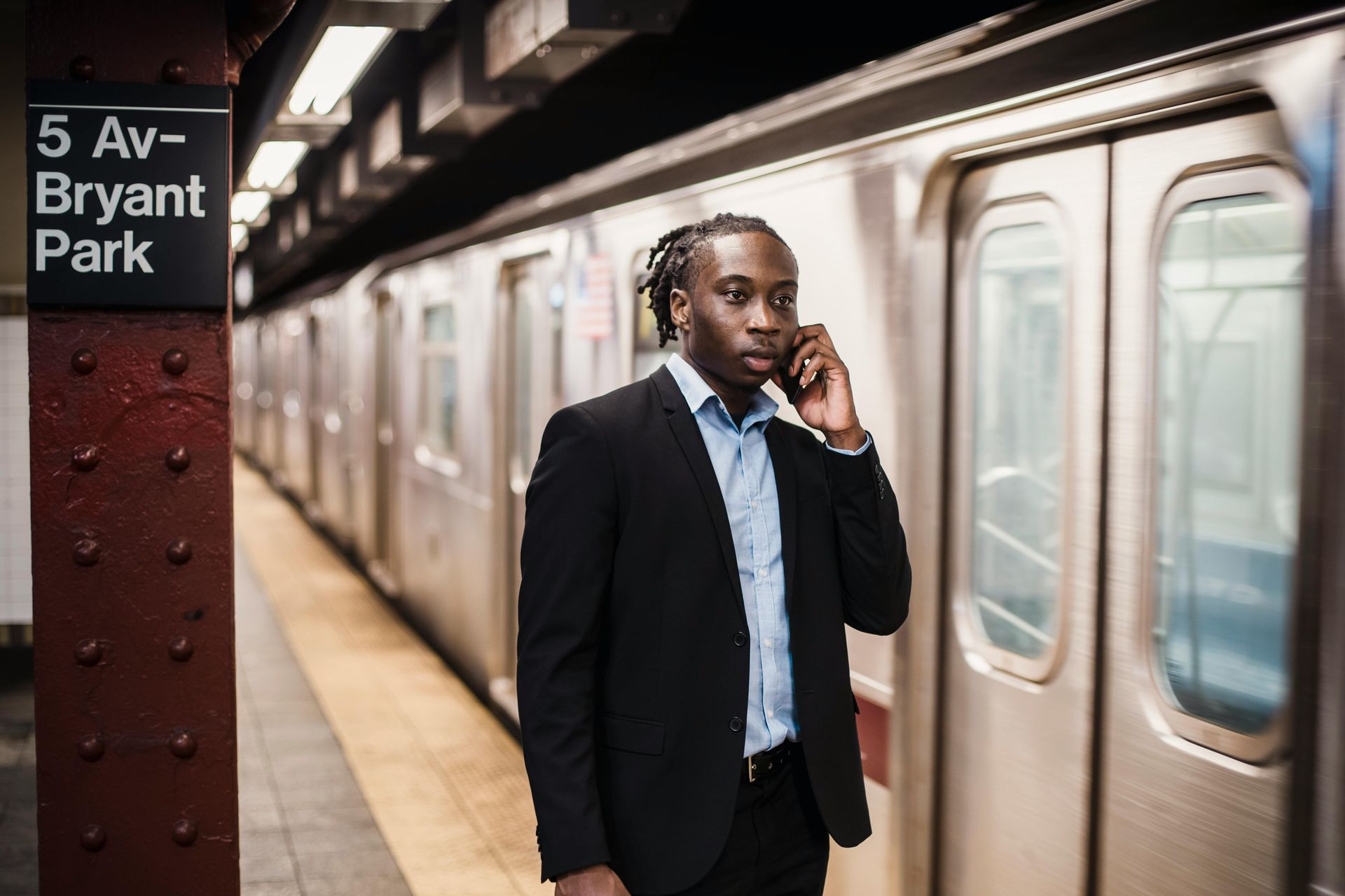 A man in a suit is talking on a cell phone in front of a train at bryant park