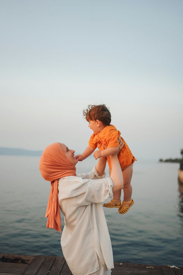 A woman is holding a baby in her arms in front of a body of water.