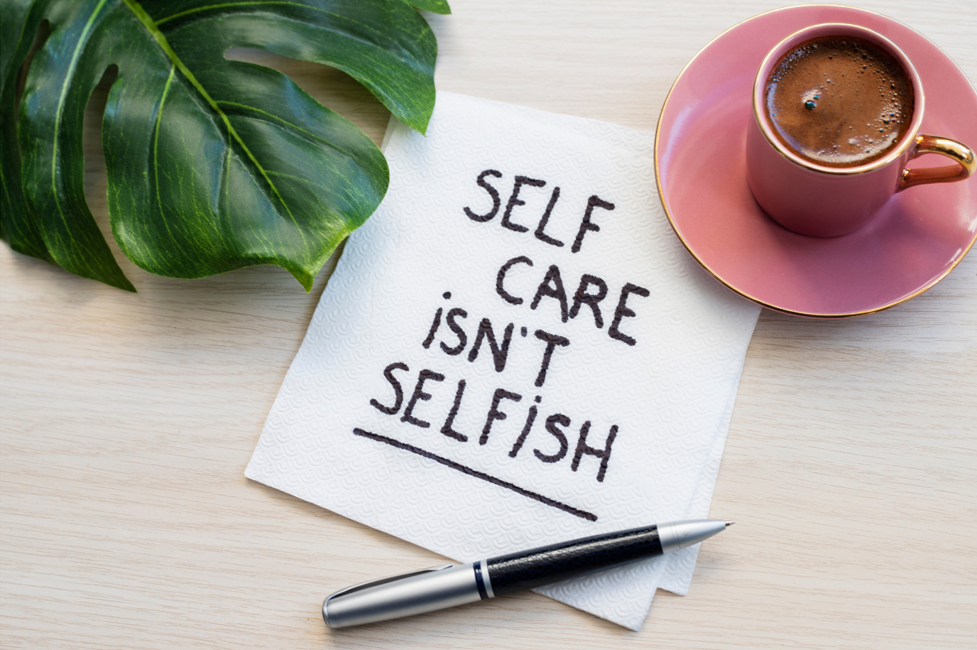 Self-care isn't selfish written on tissue paper with a pen, a cup of chocolate, and Monstera leaf.