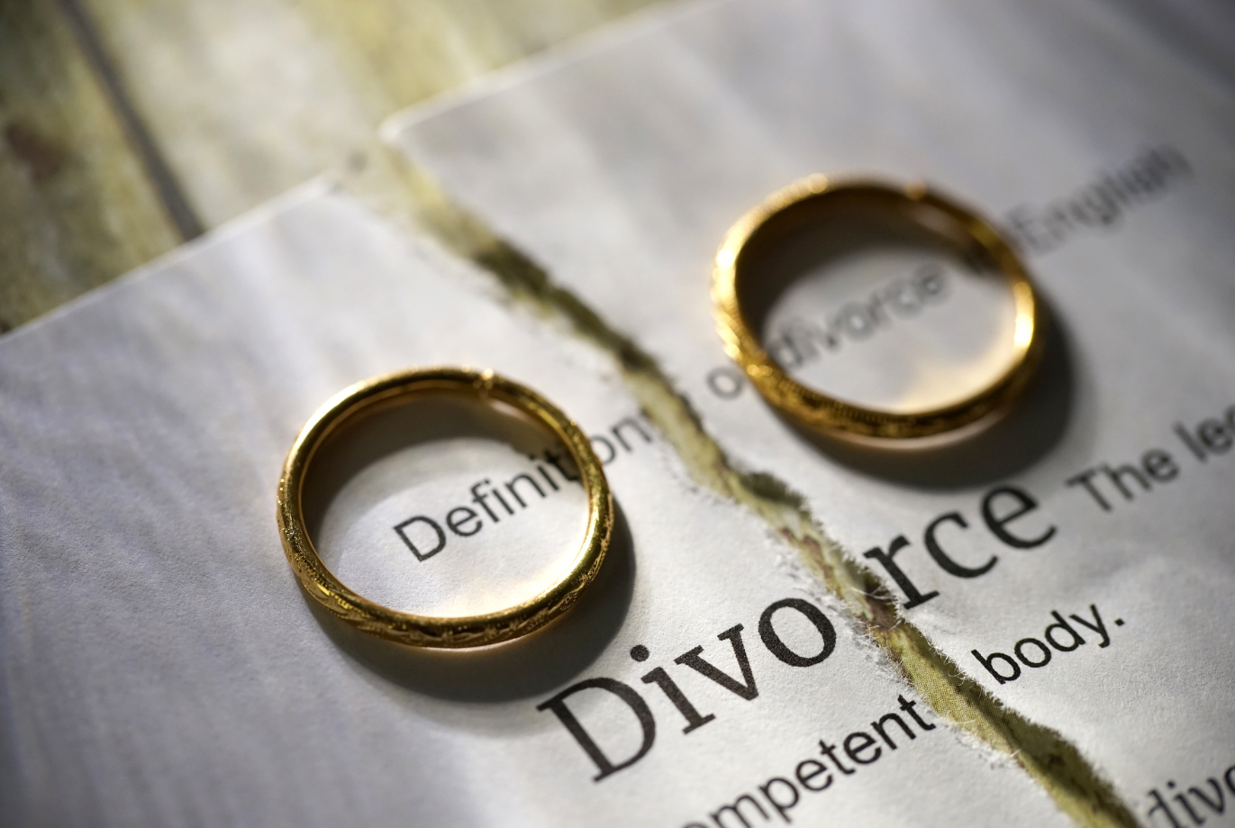 Wedding rings placed on top of a torn document printed with definition of divorce.