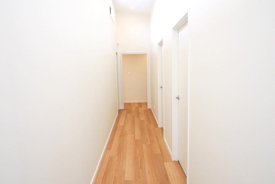 A bright, narrow hallway with light wood-patterned flooring, white walls, and several closed white doors.