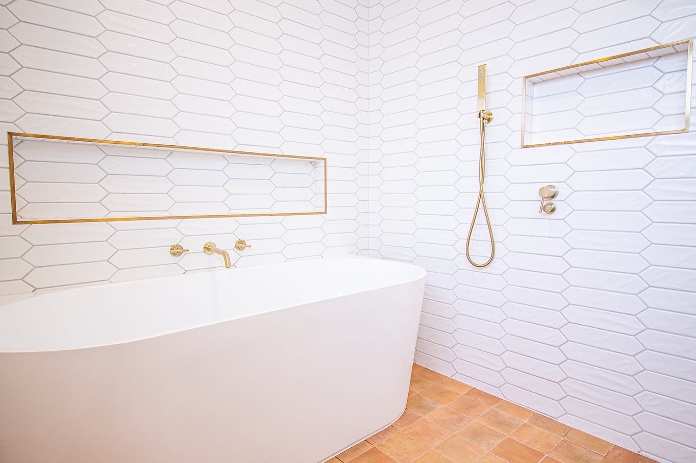 Modern bathroom with a white freestanding tub, gold fixtures, recessed wall niches, and white picket-tile walls.