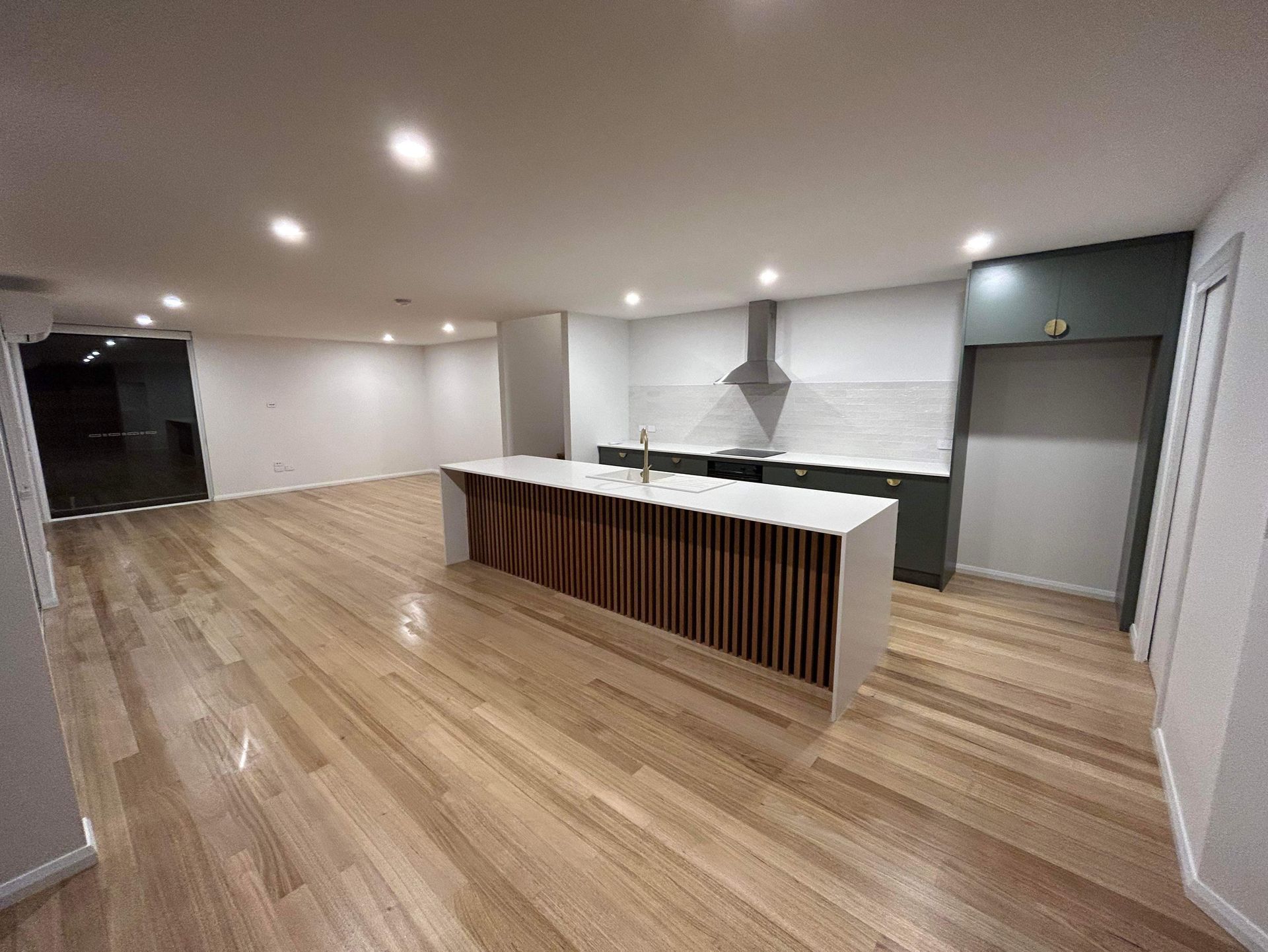 Modern open-plan kitchen with a wooden slatted island, white countertops, and light hardwood flooring.