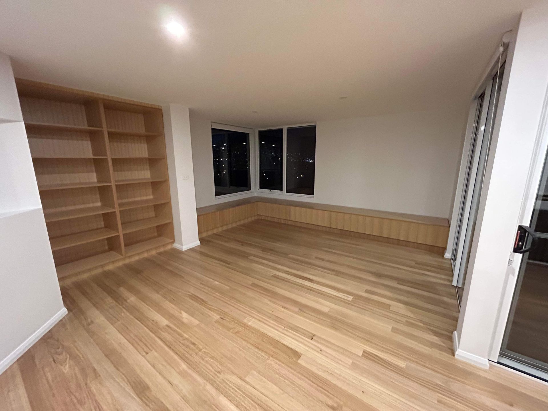 An unfurnished room featuring light wood flooring, a built-in wooden bookshelf, and a low window bench seat.