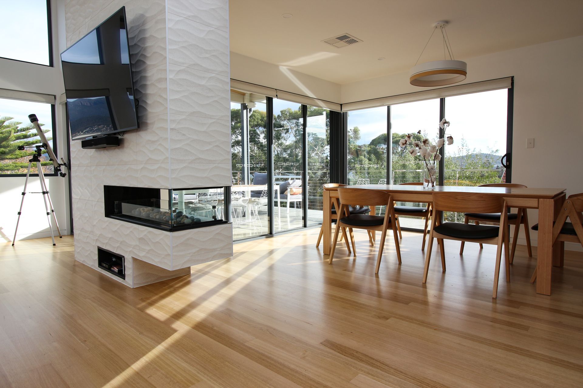 A modern dining area with hardwood floors, a white brick fireplace feature wall, a mounted TV, and large glass windows.