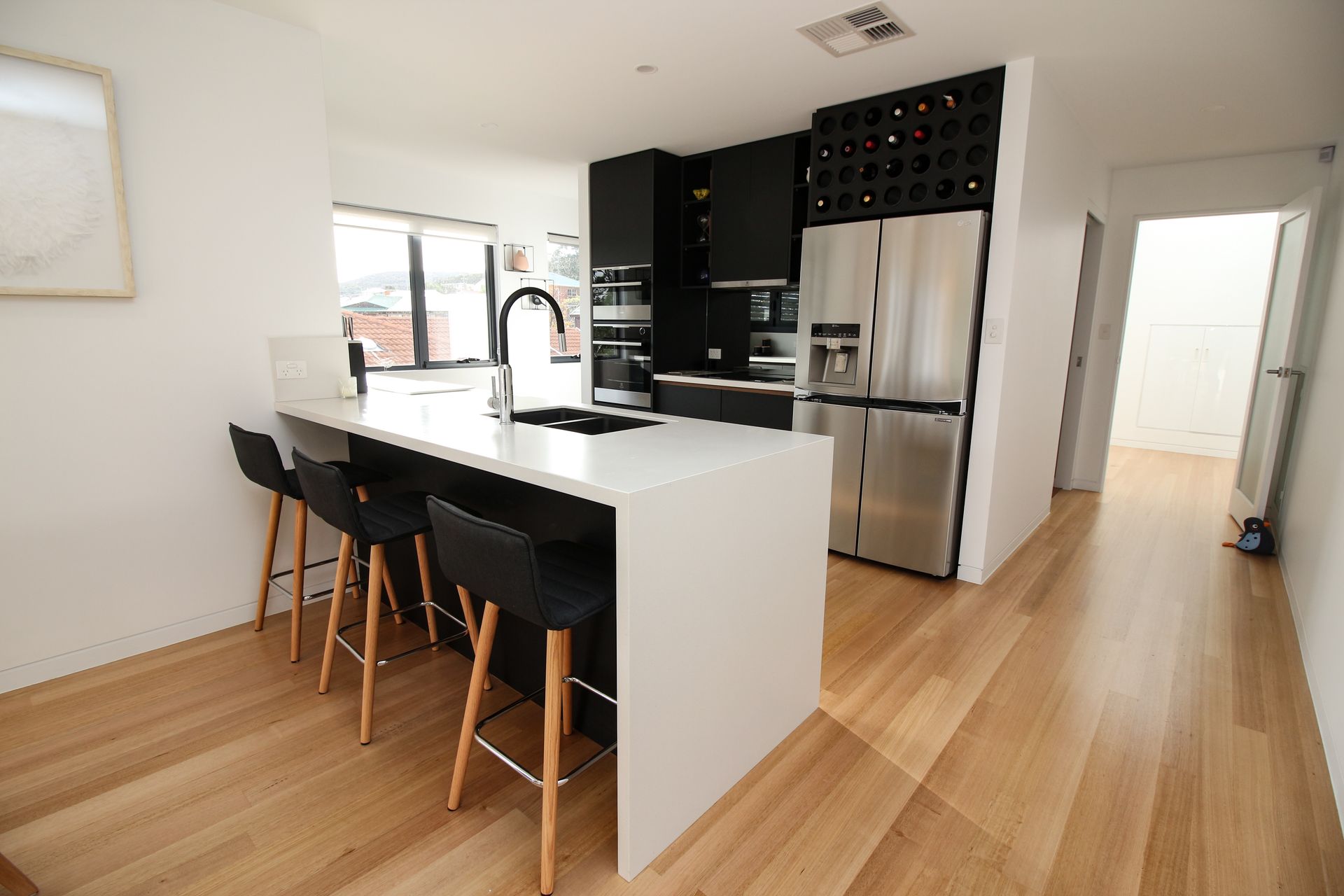 A modern kitchen with white counters, a black kitchen island with three bar stools, and stainless steel appliances.