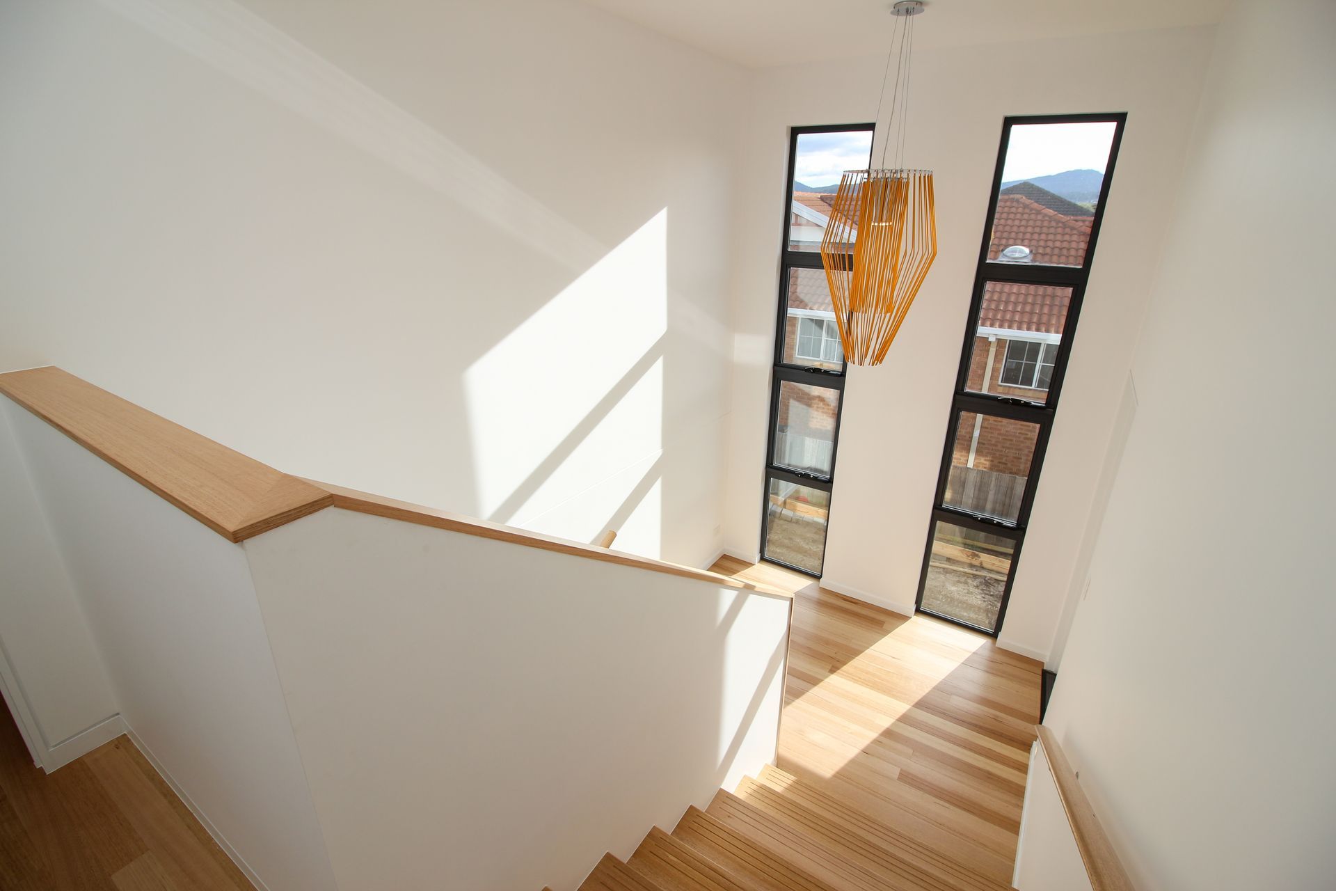 A wooden staircase with white walls, illuminated by bright sunlight streaming through two tall, vertical windows.