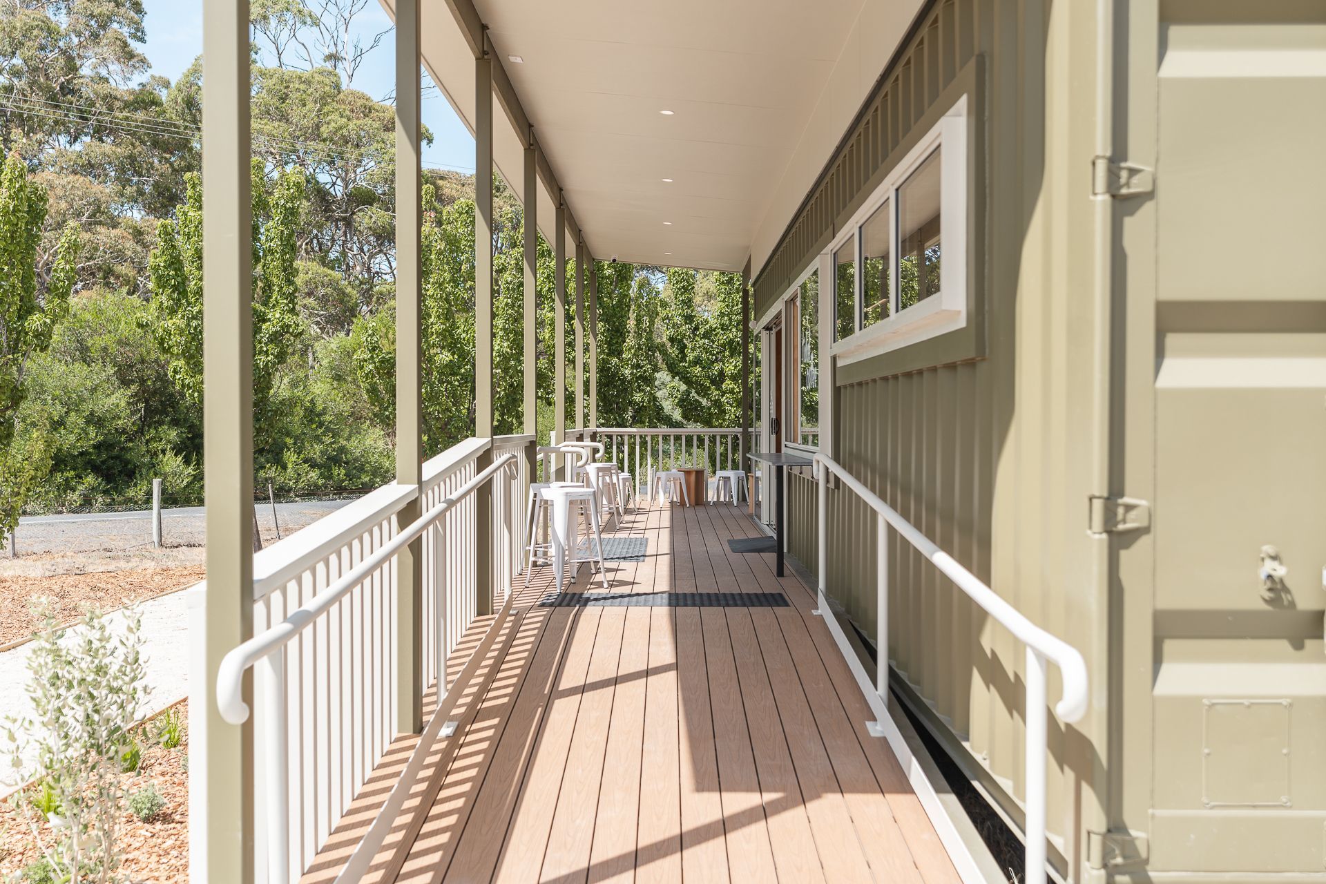 A wheelchair-accessible ramp with white railings leads along the side of a modern, sage green shipping container home.