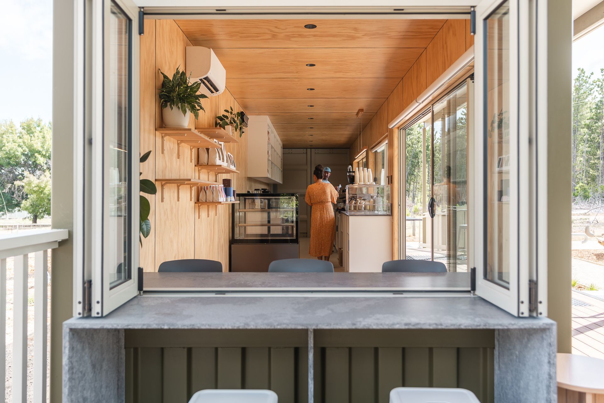 A view from a concrete bar looking into a wooden-paneled cafe with a person standing at a counter.