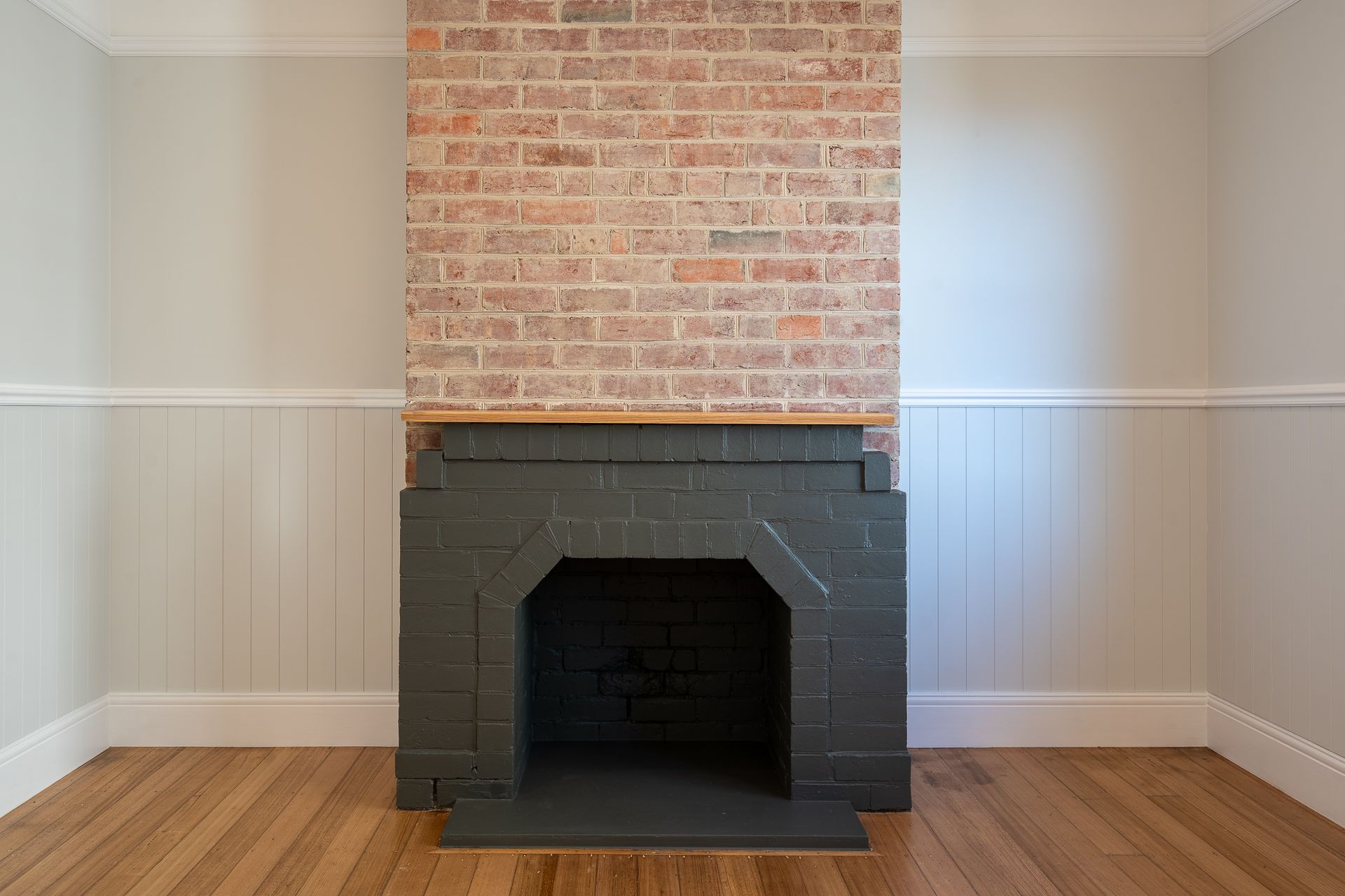 A fireplace with a painted dark grey brick hearth and surround, set against a natural exposed brick chimney and wood floors.