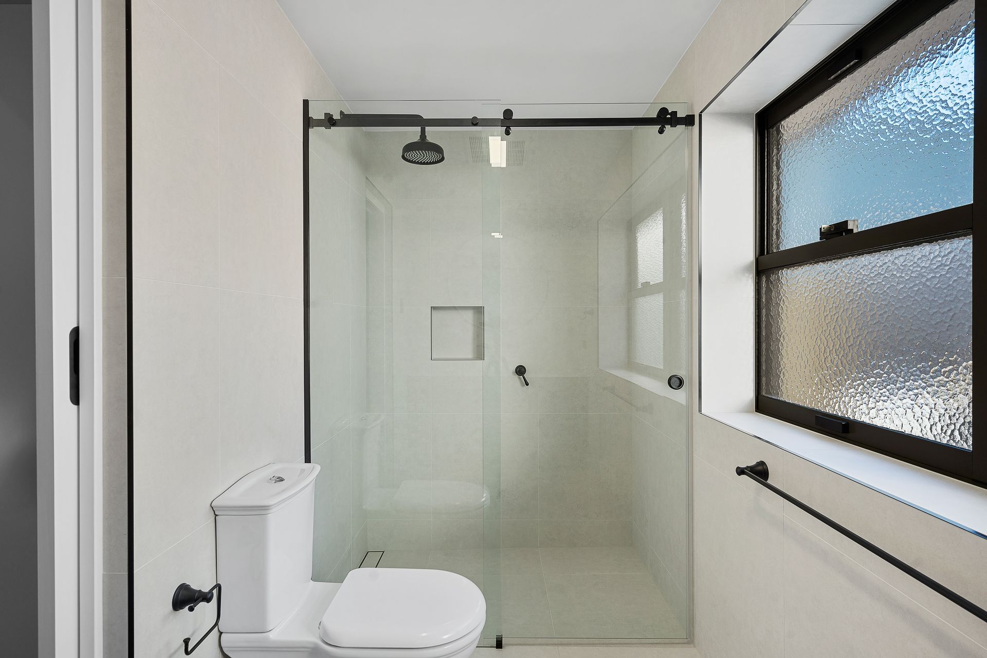 Modern bathroom with a white toilet and a glass-enclosed walk-in shower featuring black hardware and a frosted window.