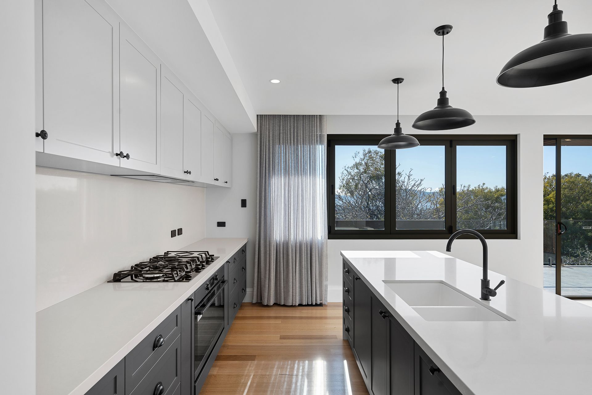 A modern kitchen featuring dark lower cabinets, white upper cabinets, white quartz countertops, and three pendant lights.