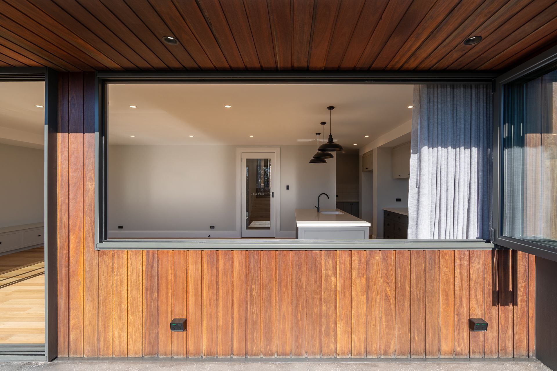 View through an open window into a bright, modern interior with wood-paneled exterior walls and ceiling.
