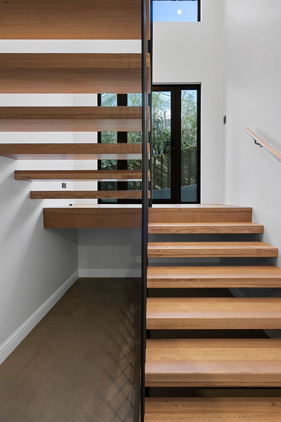 Floating wooden staircase in a modern home with white walls and a large window.