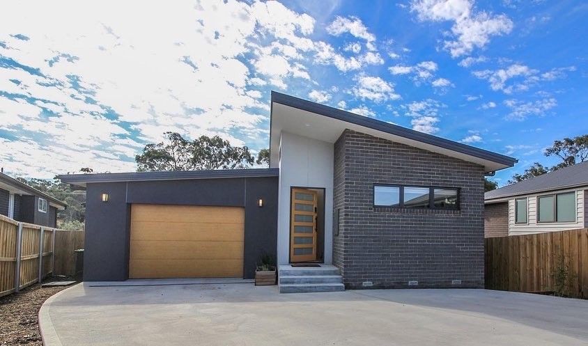 Modern home exterior with a dark gray garage, textured charcoal brick siding, wooden front door, and concrete driveway.