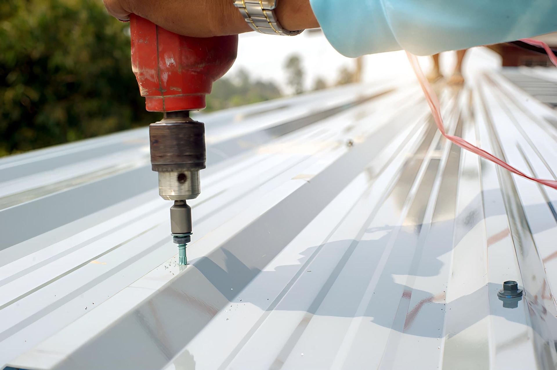 Man is Using a Drill to Drill a Hole in a Metal Roof — Above All Roof Painters & Repairs in Bellmere, QLD