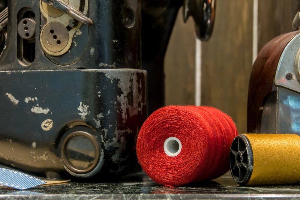 A Spool Of Red Thread Is Sitting On A Table Next To A Sewing Machine — The Sewing Machine Doctor In Forest Glen, QLD