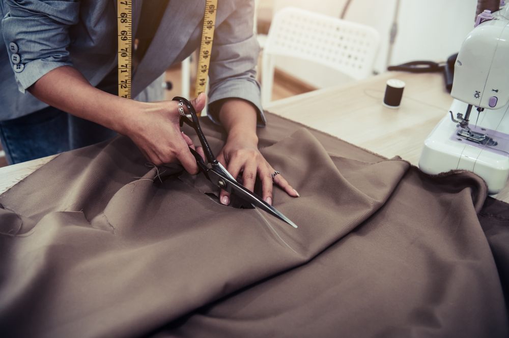 A Woman Is Cutting A Piece Of Fabric With Scissors — The Sewing Machine Doctor In Forest Glen, QLD