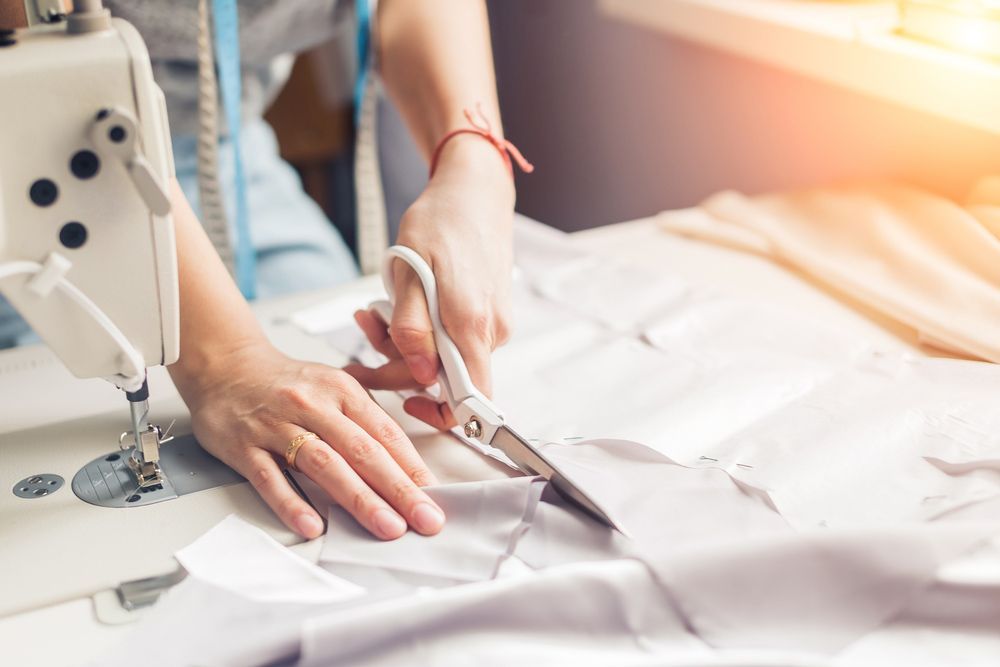 A Woman Is Cutting Fabric With Scissors On A Sewing Machine — The Sewing Machine Doctor In Forest Glen, QLD