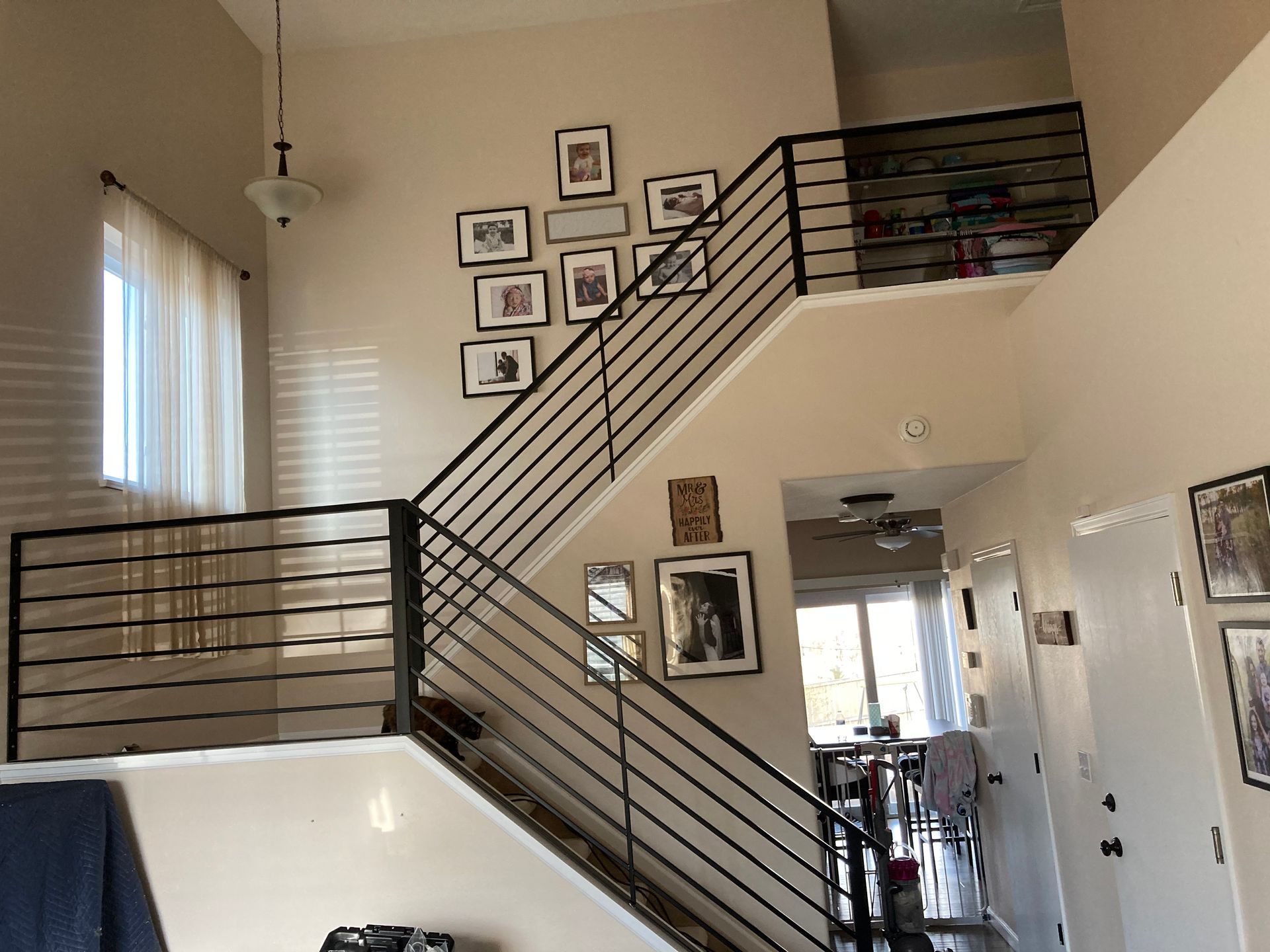 Two-story staircase with black railing, art on the wall, and a window with curtains.