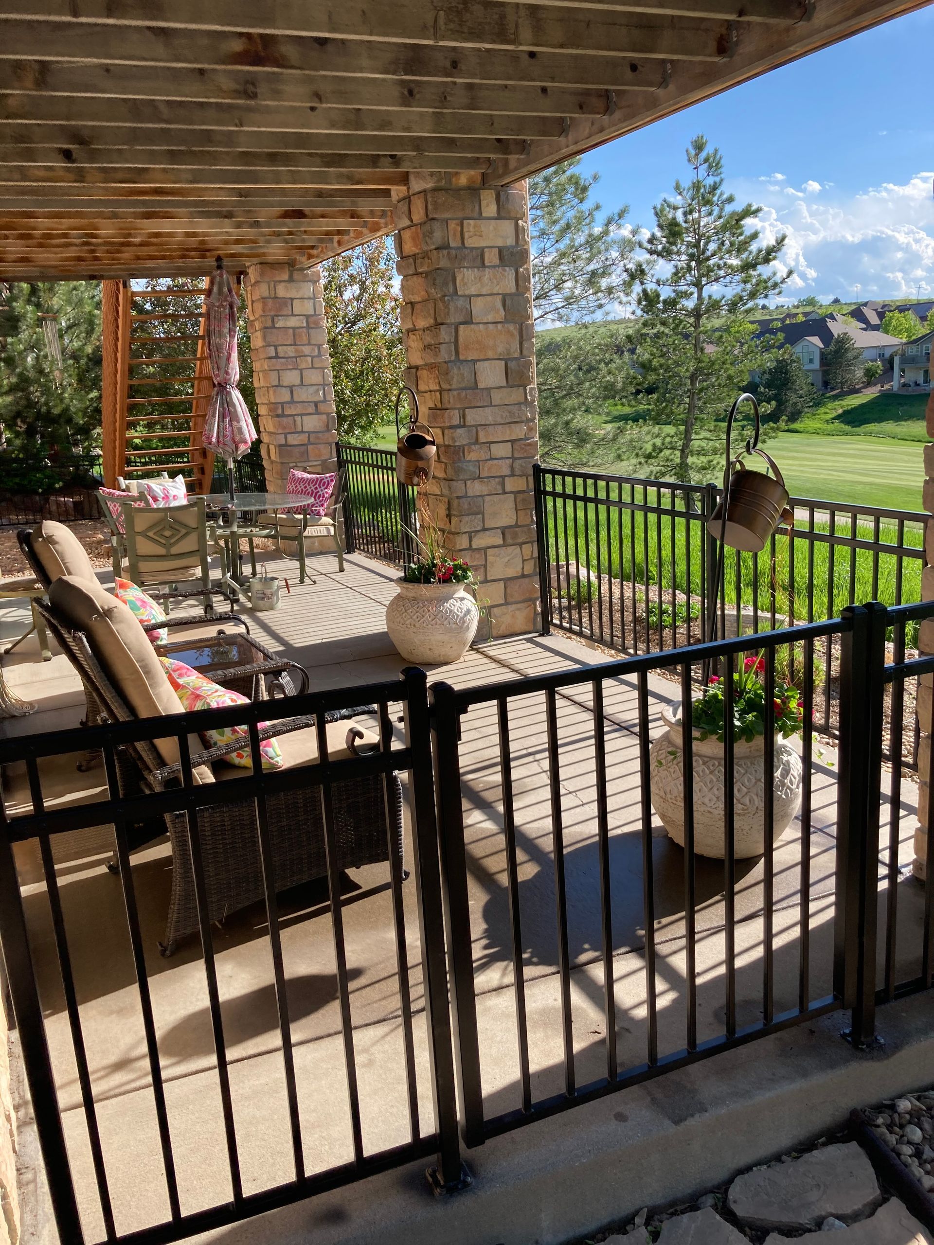 Patio with stone columns, wrought iron railing, and potted plants overlooking a green yard.