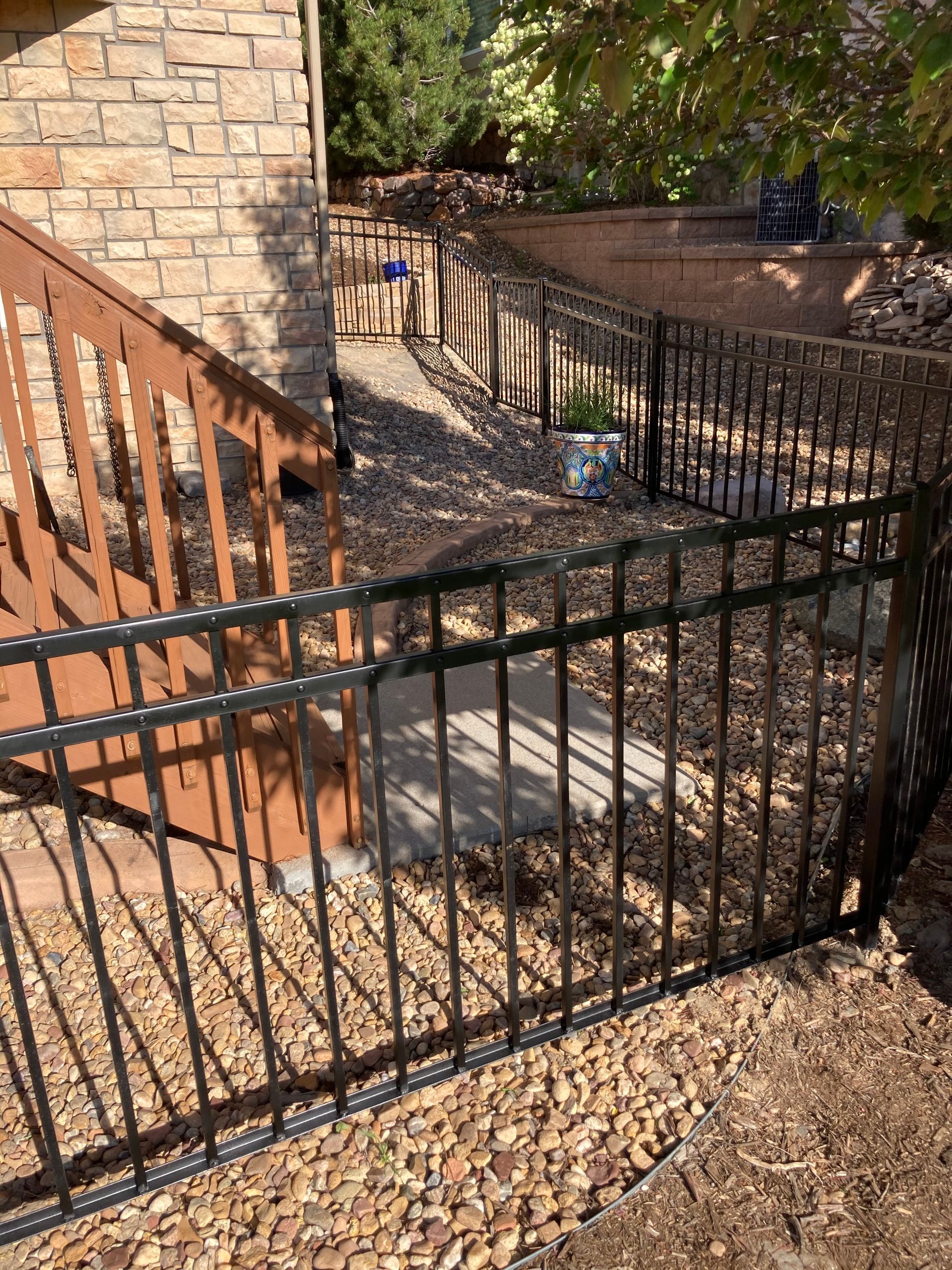 Black metal fence surrounding a pathway near a brick building and a brown wooden staircase.