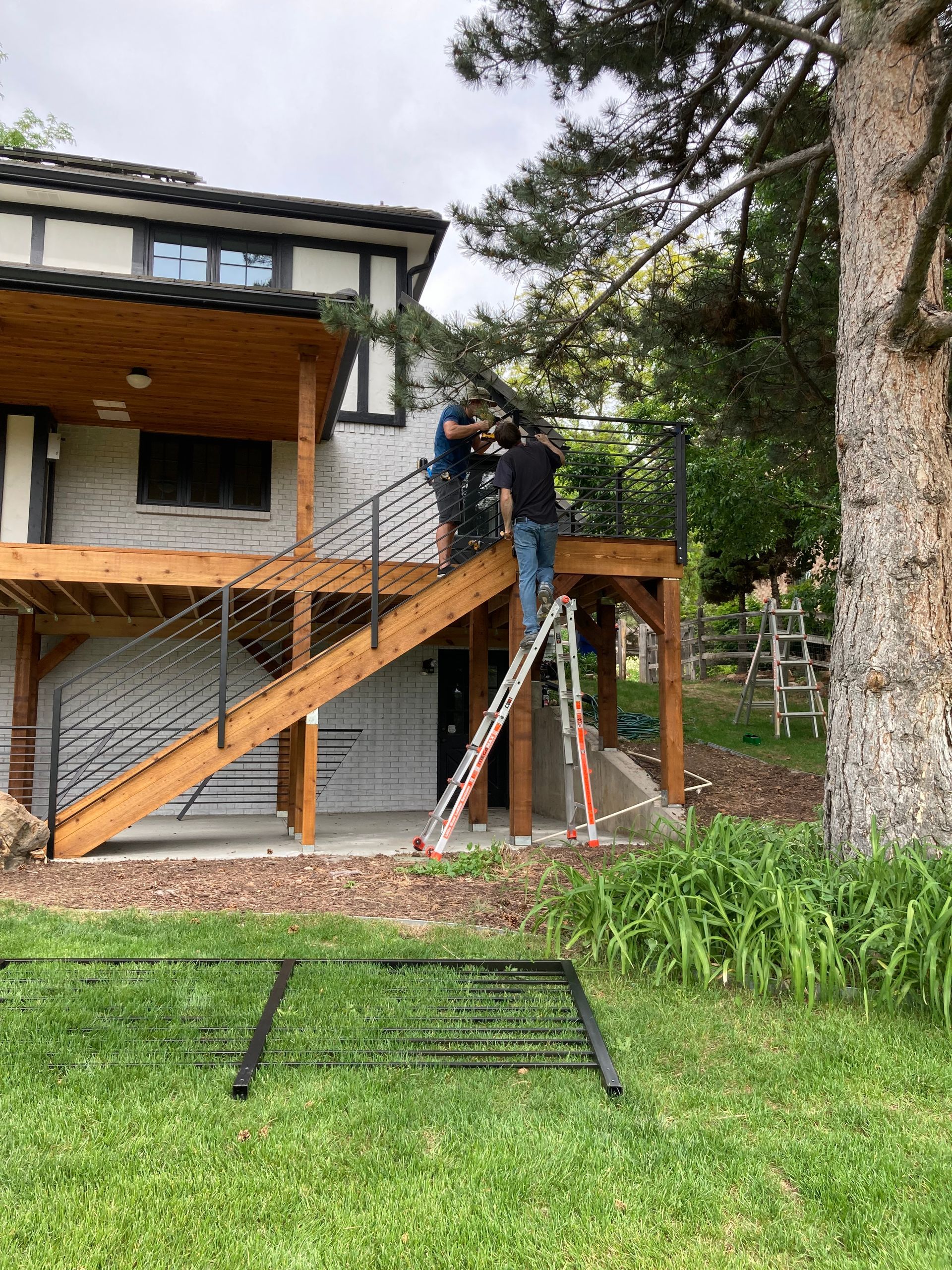 Two people install railing on a wood deck and stairs of a two-story home.