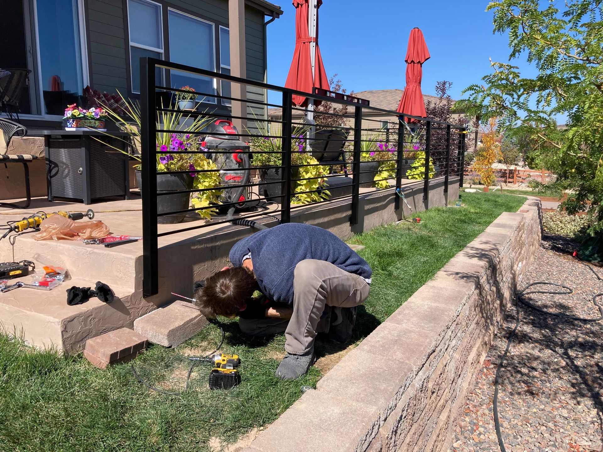 Person installing a black railing near a patio with red umbrellas.