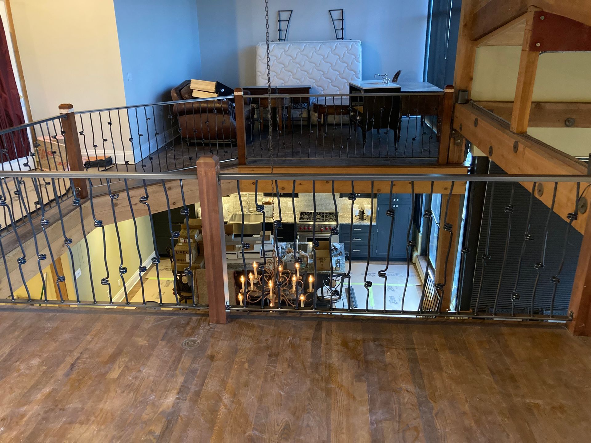 Loft interior: wrought iron railing, wood floor, open kitchen below, seating area with furniture.