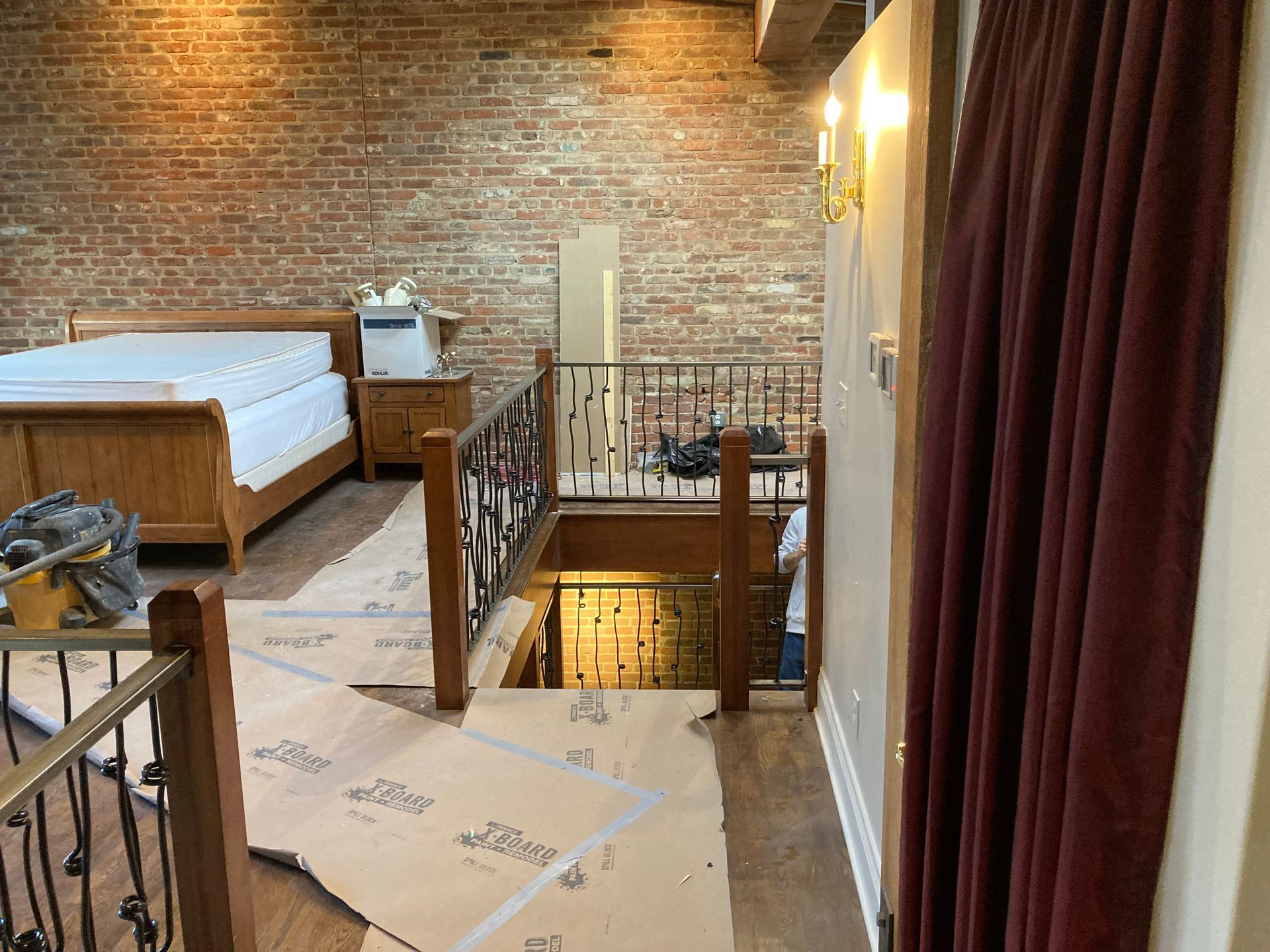 Bedroom with exposed brick wall, wooden furniture, and a staircase leading down.
