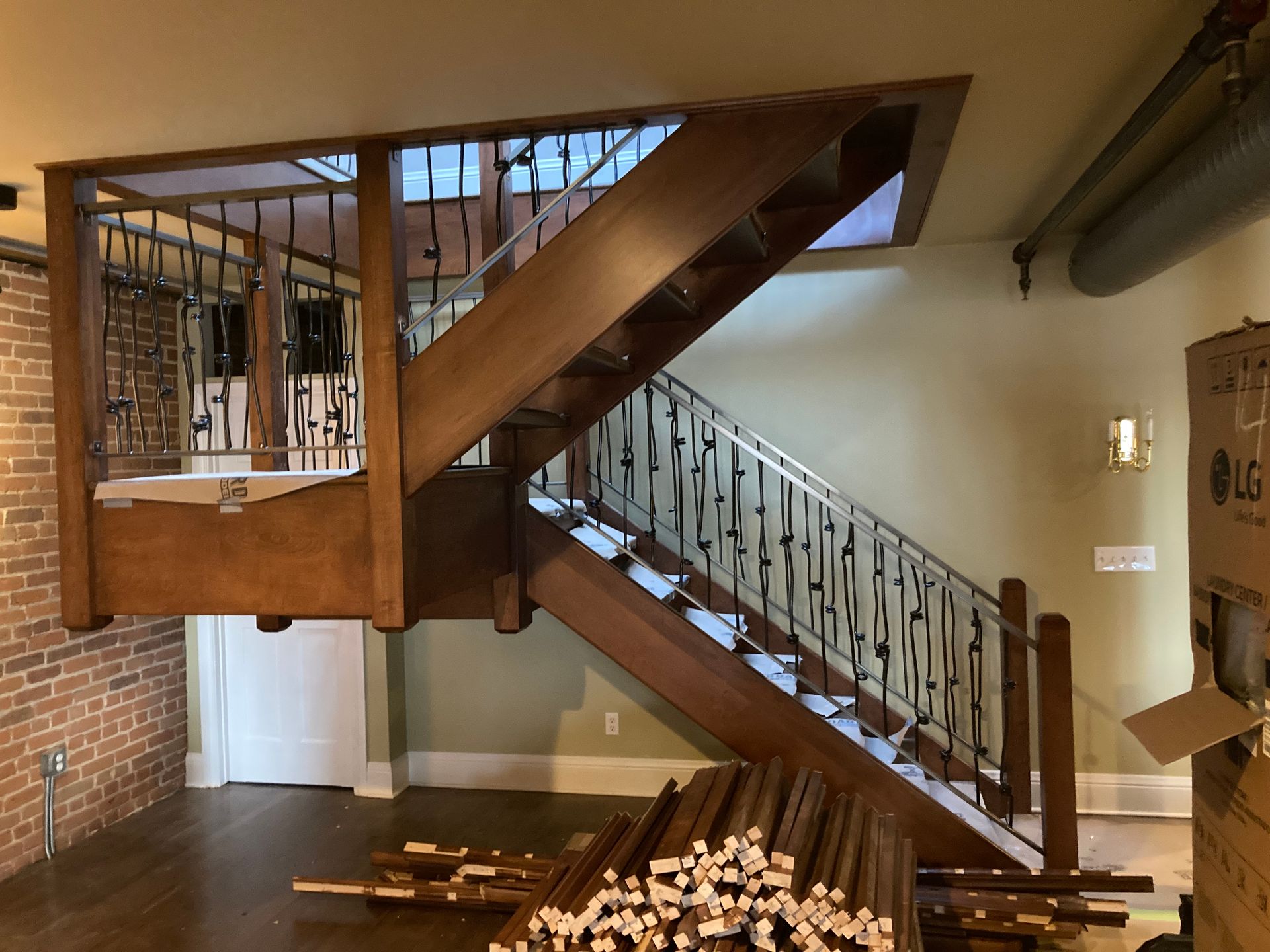 Wooden staircase with decorative iron railing in a renovated space; materials on floor.