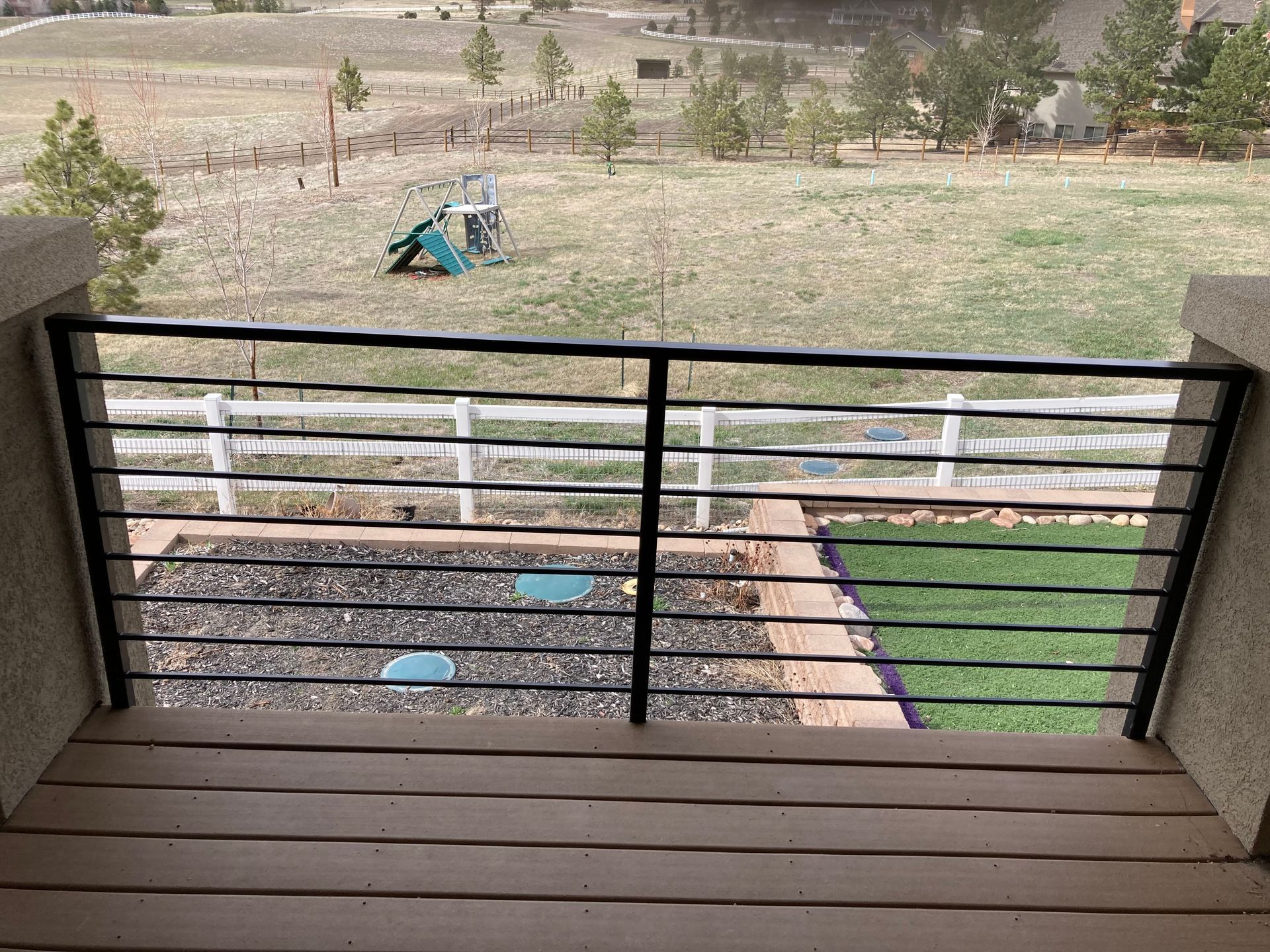 Black metal railing on a deck overlooking a yard with a white fence and a playground.