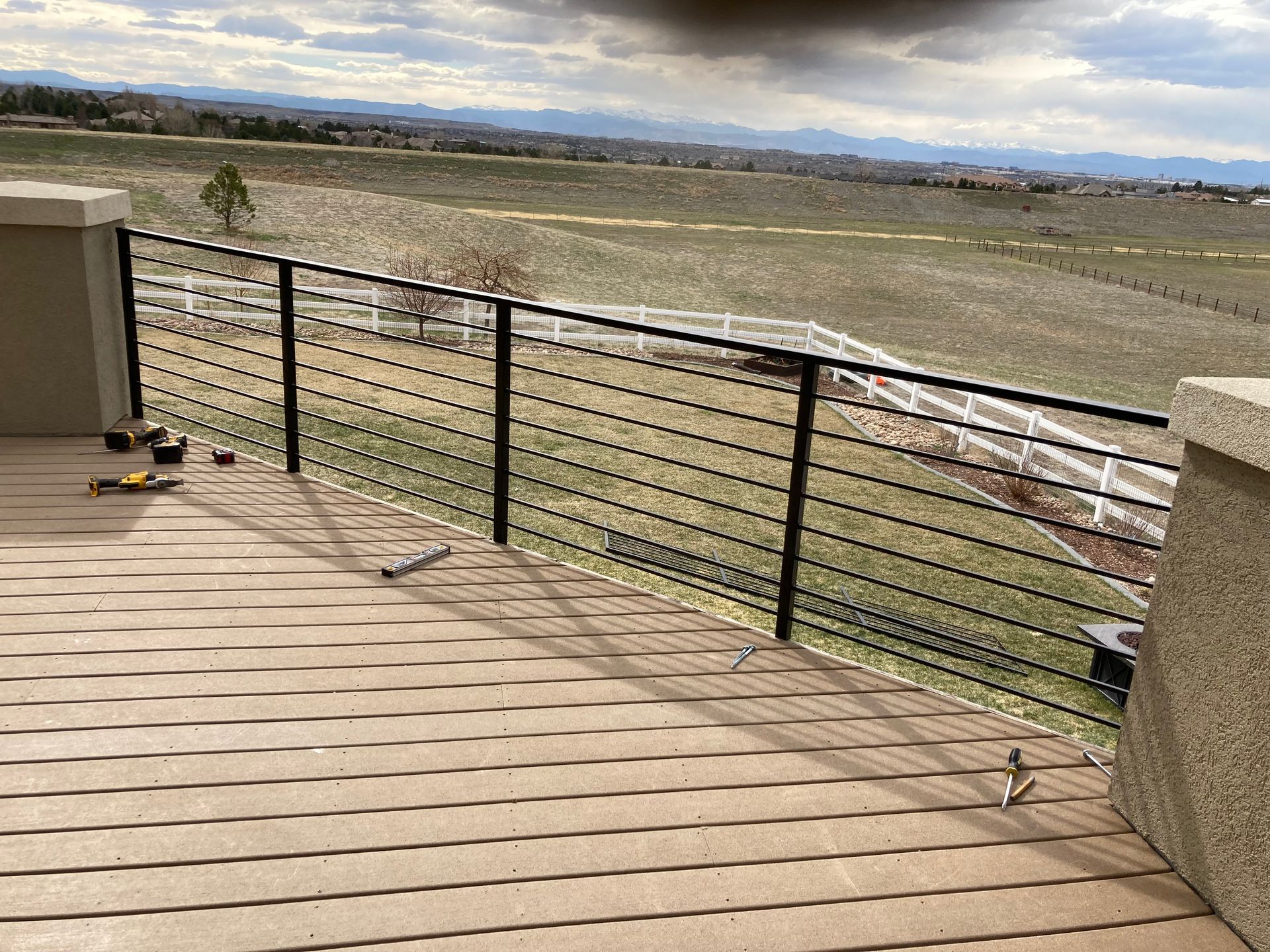 Black metal cable railing on a deck overlooking a rural landscape under a cloudy sky.