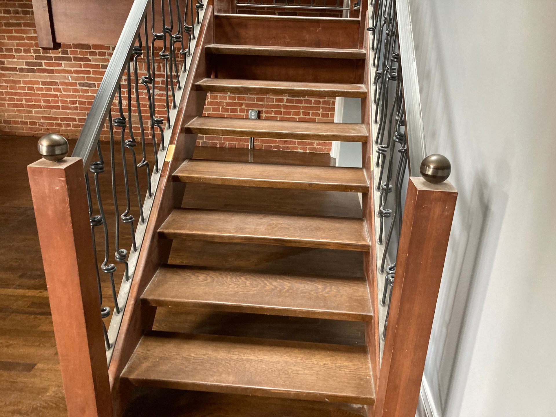 Wooden staircase with metal railings and brick wall backdrop.