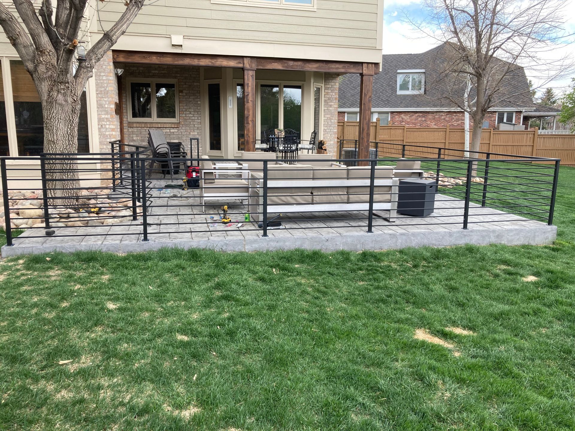 A backyard patio with a black metal railing, concrete steps, and a green lawn.
