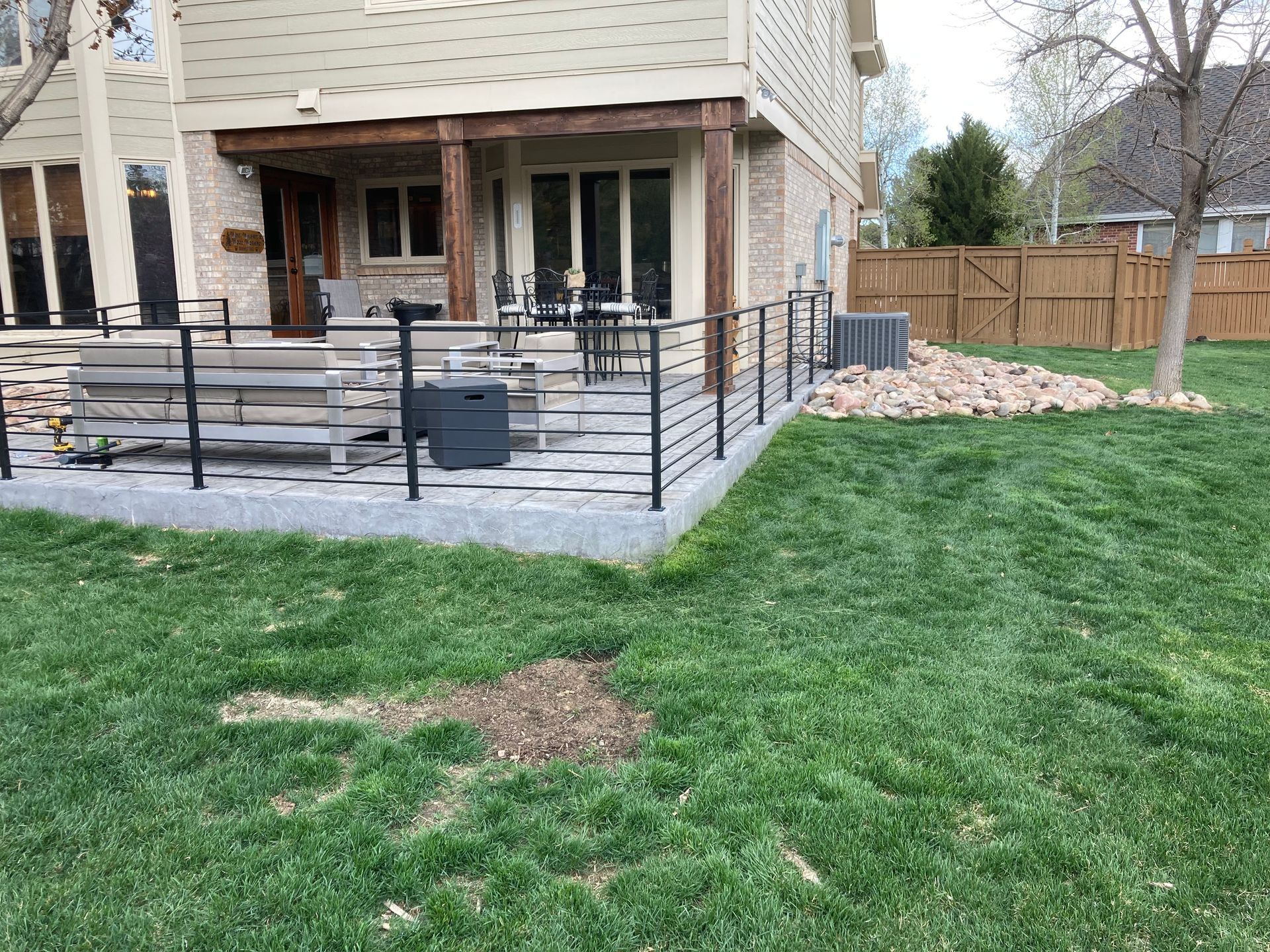 A patio with black railing and a stone base, next to green grass and a house.