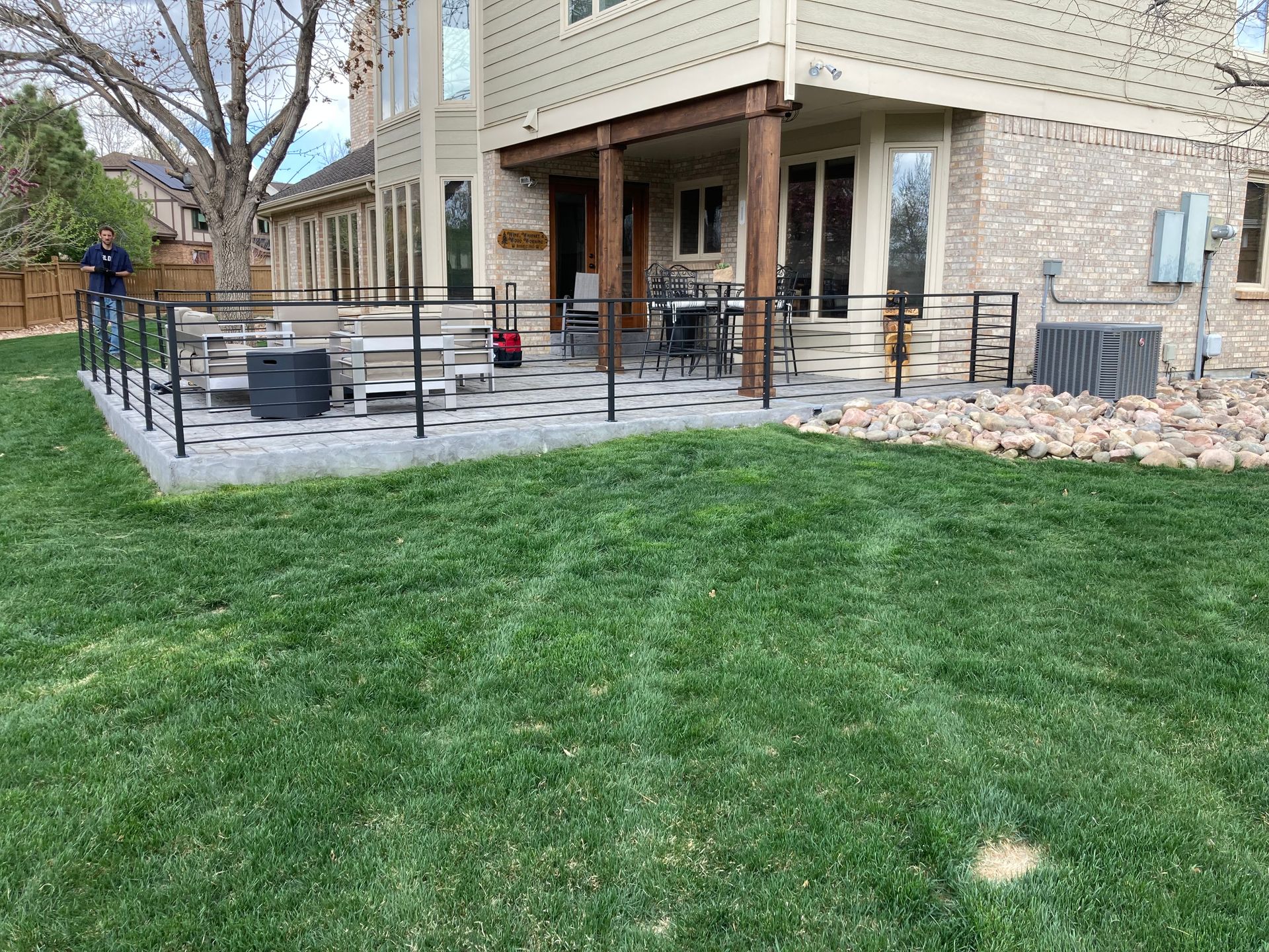 Backyard patio with black railing, gray pavers, and a lawn with green grass.