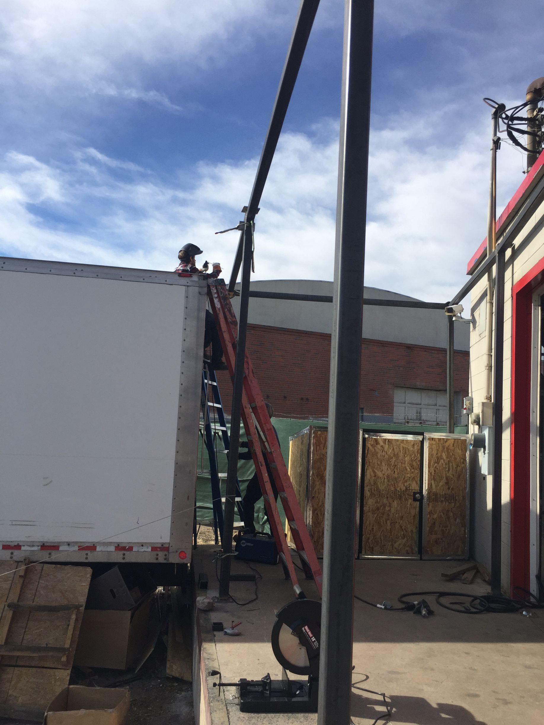 Person on truck roof near an elevated ladder, next to a building and utility pole, outdoors.