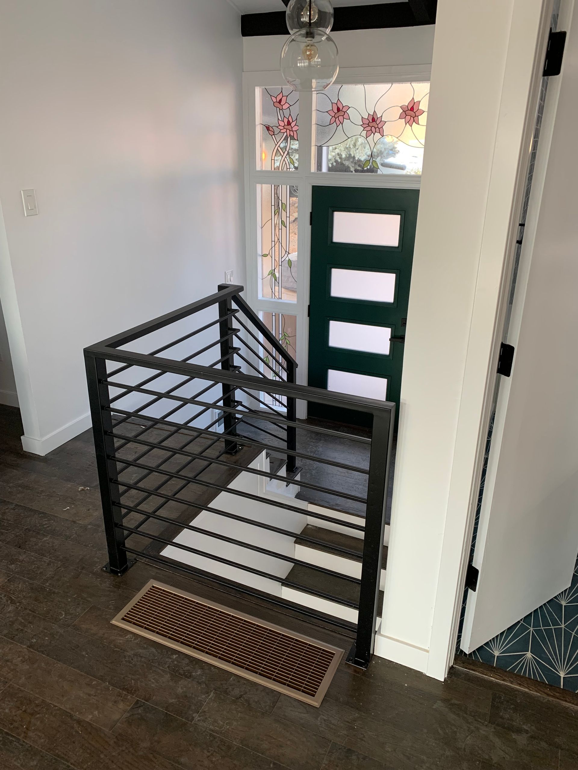 Entryway with black railing, white and black stairs, green door, and white trim.