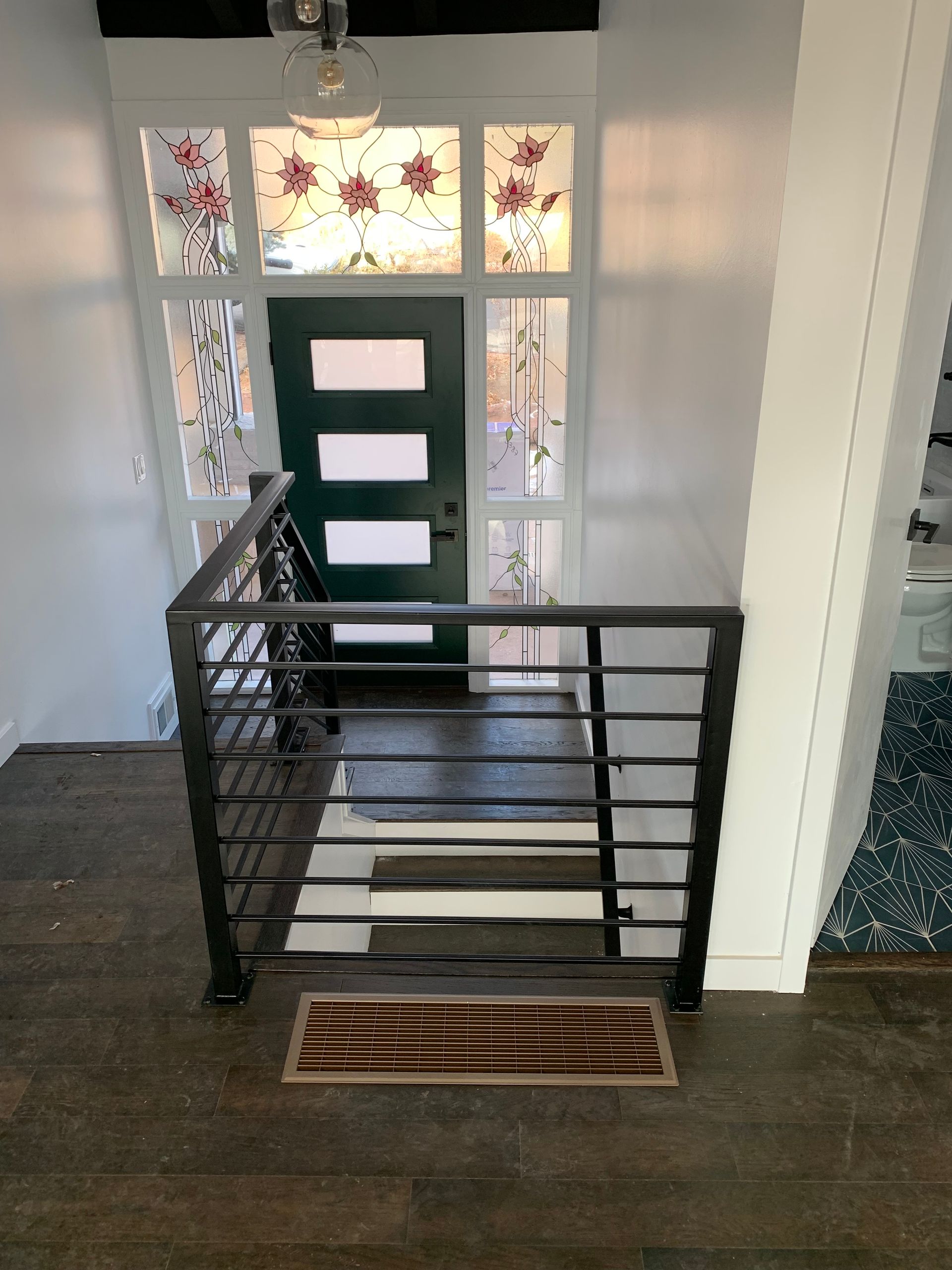 Dark metal stair railing in front of a green door with frosted windows and decorative floral design.