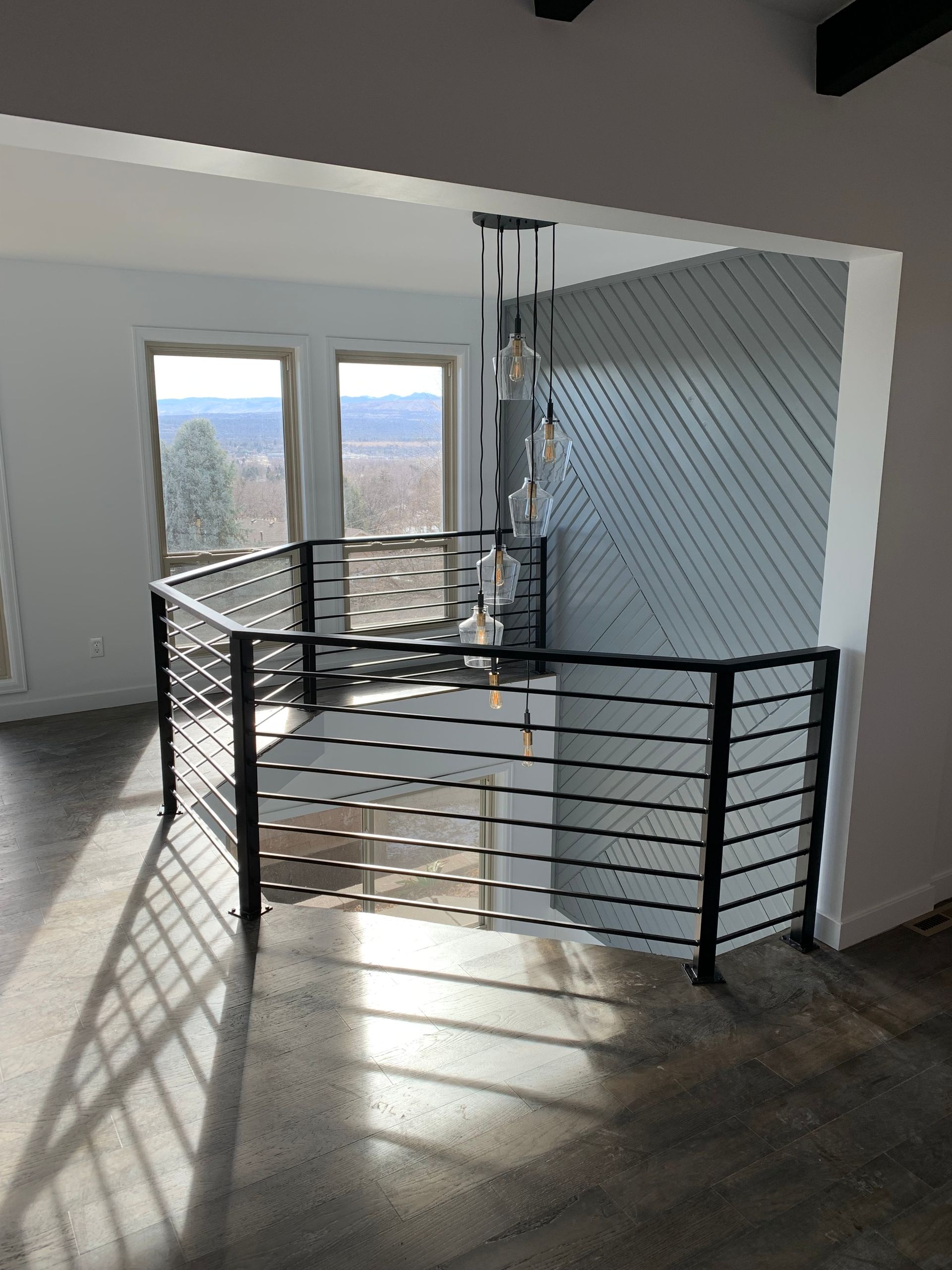 Staircase with black metal railing, light wood steps, and matching flooring. Wall is light gray.