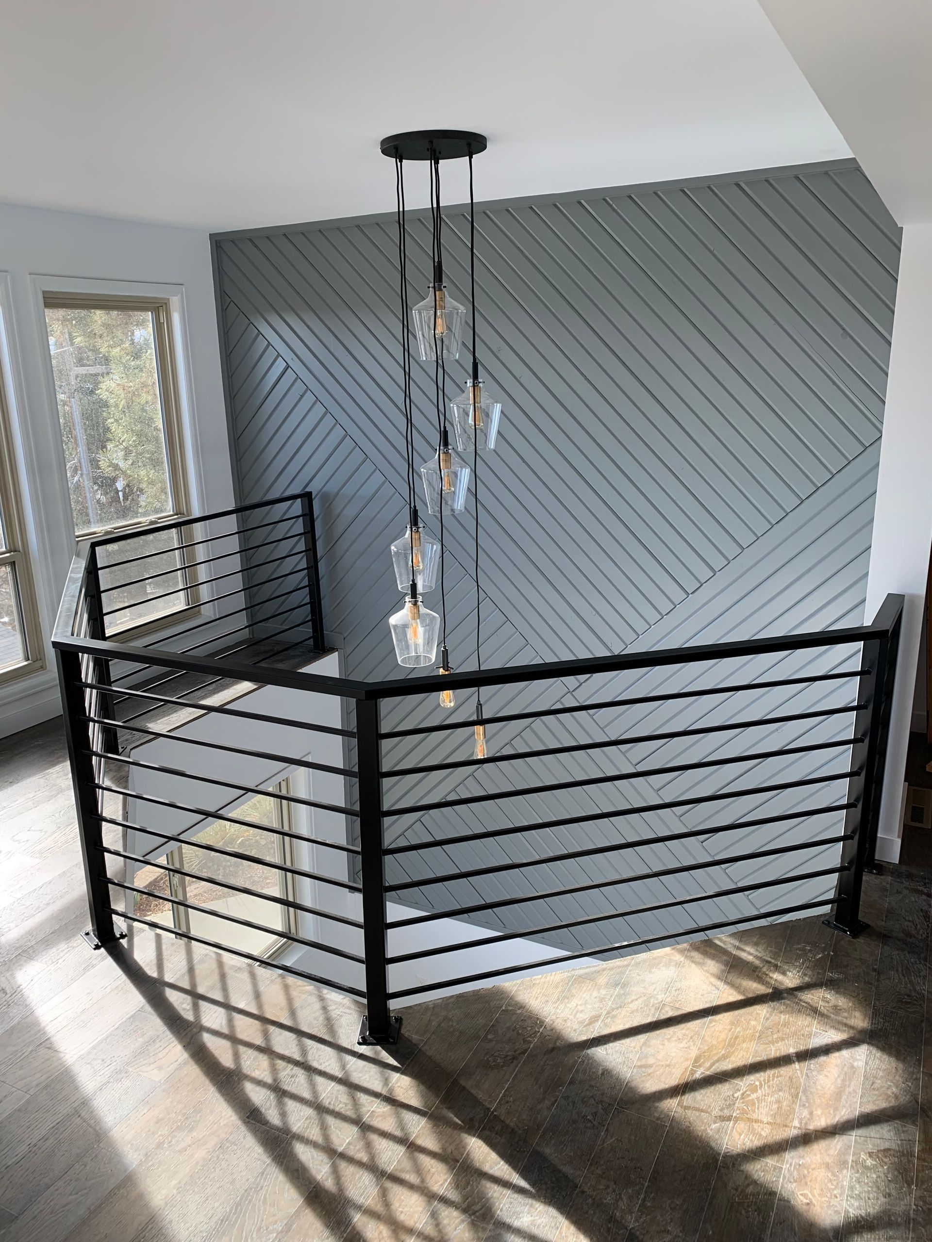 Modern staircase with black metal railings and gray accent wall, chandelier hanging.