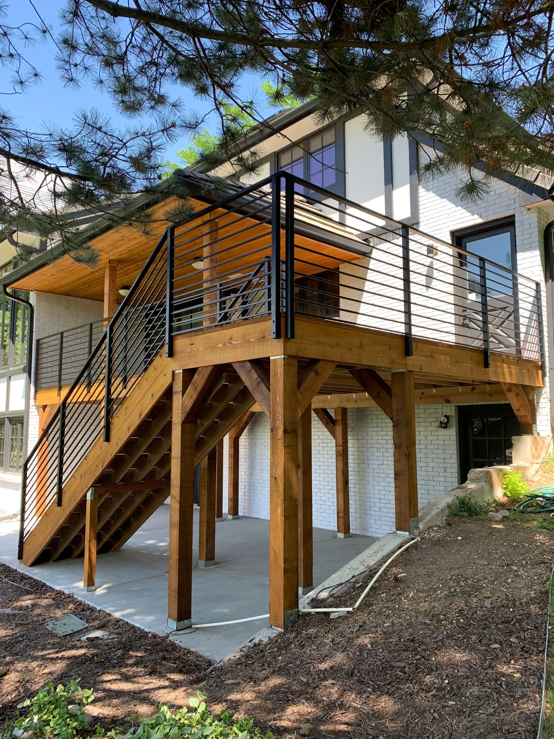 Wooden deck with black railing and stairs on a white house with a concrete patio underneath.