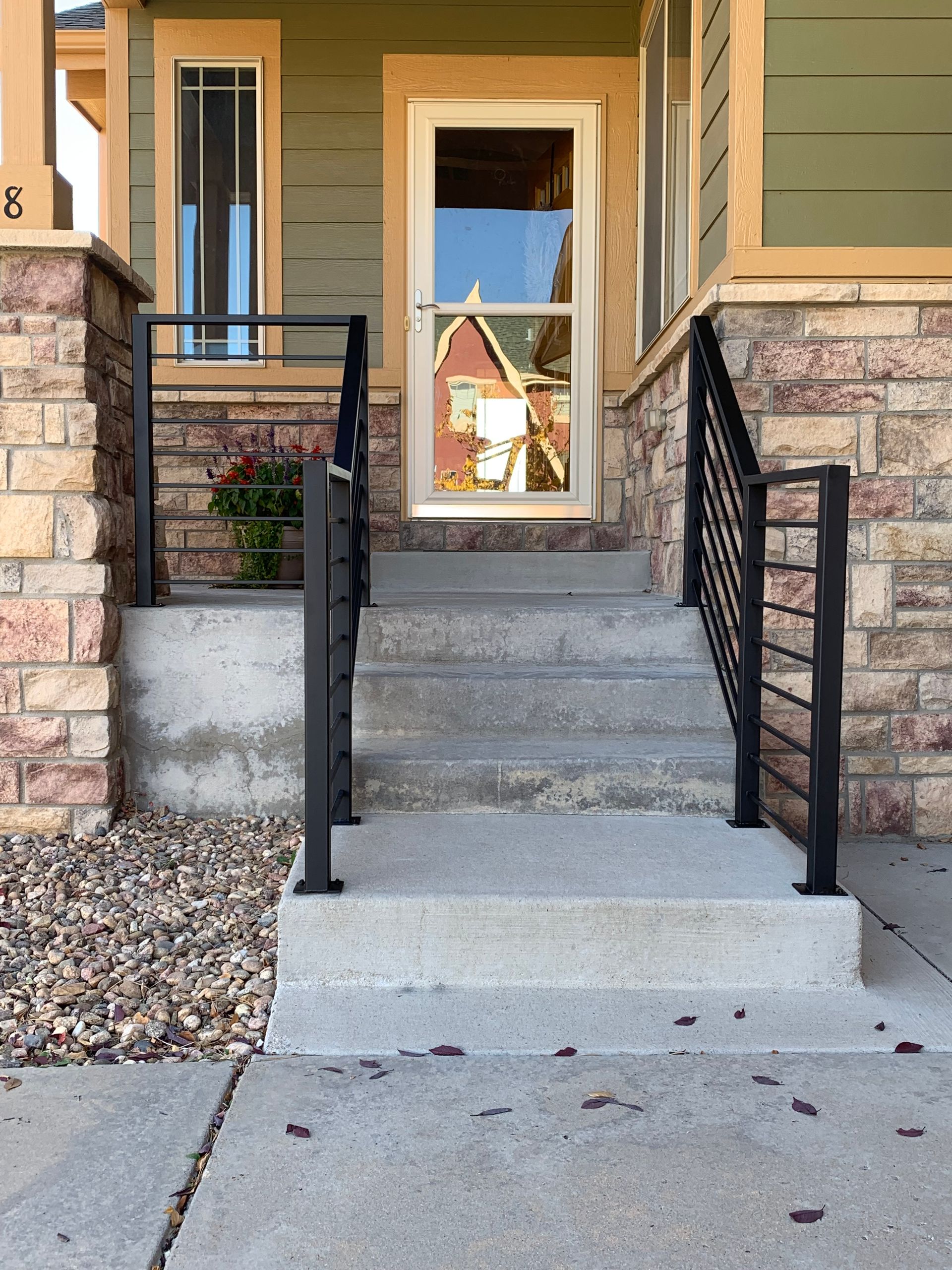 Concrete steps with black metal railings leading to a front door, flanked by brick columns.