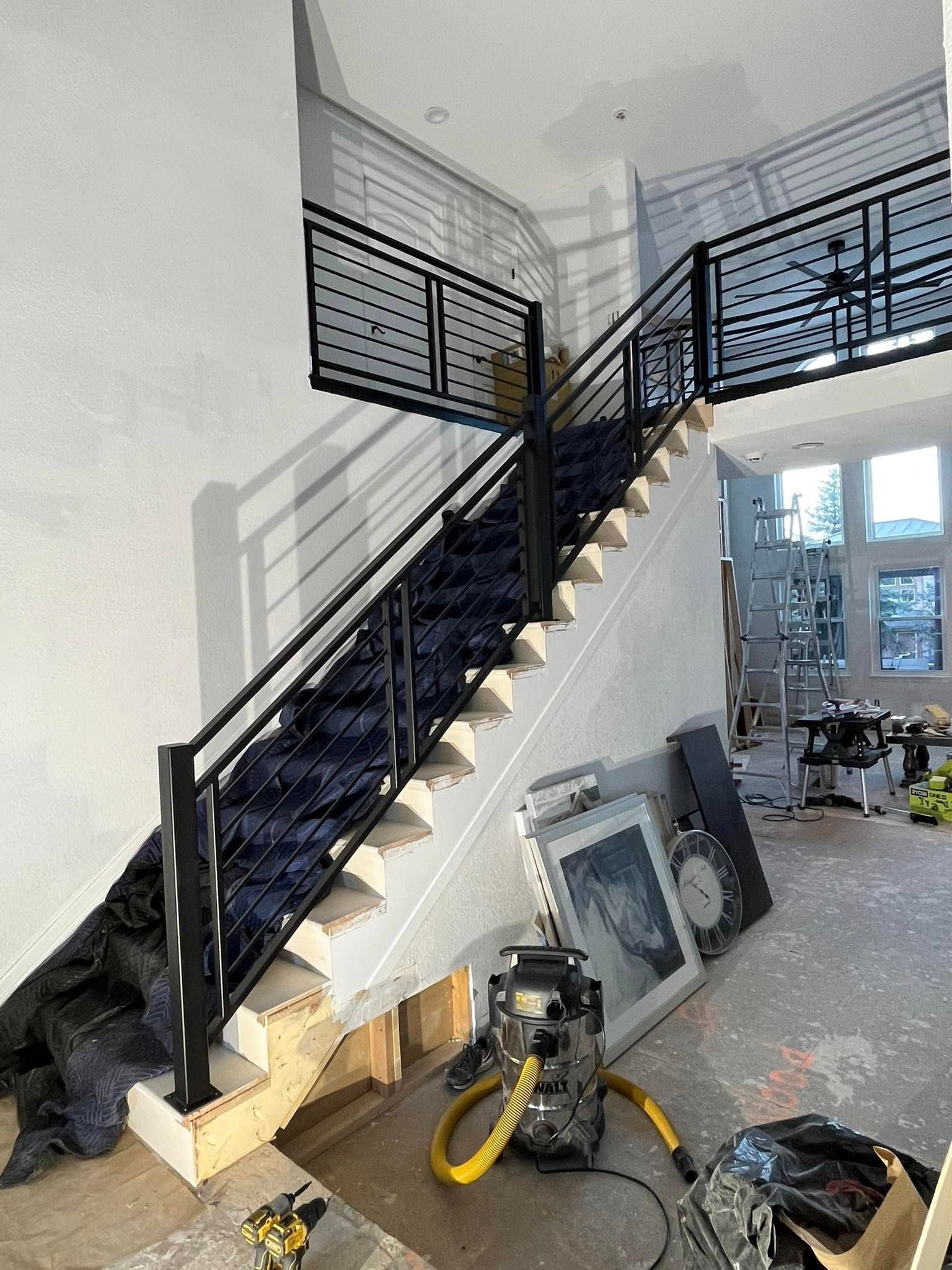 Staircase with black metal railings and a black carpet runner, construction tools visible.