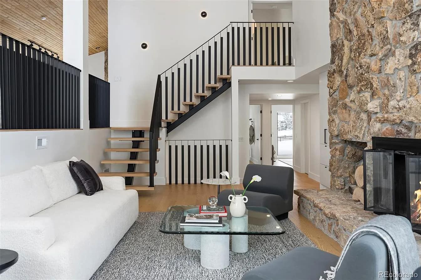 Modern living room with a stone fireplace, staircase, and white furniture.